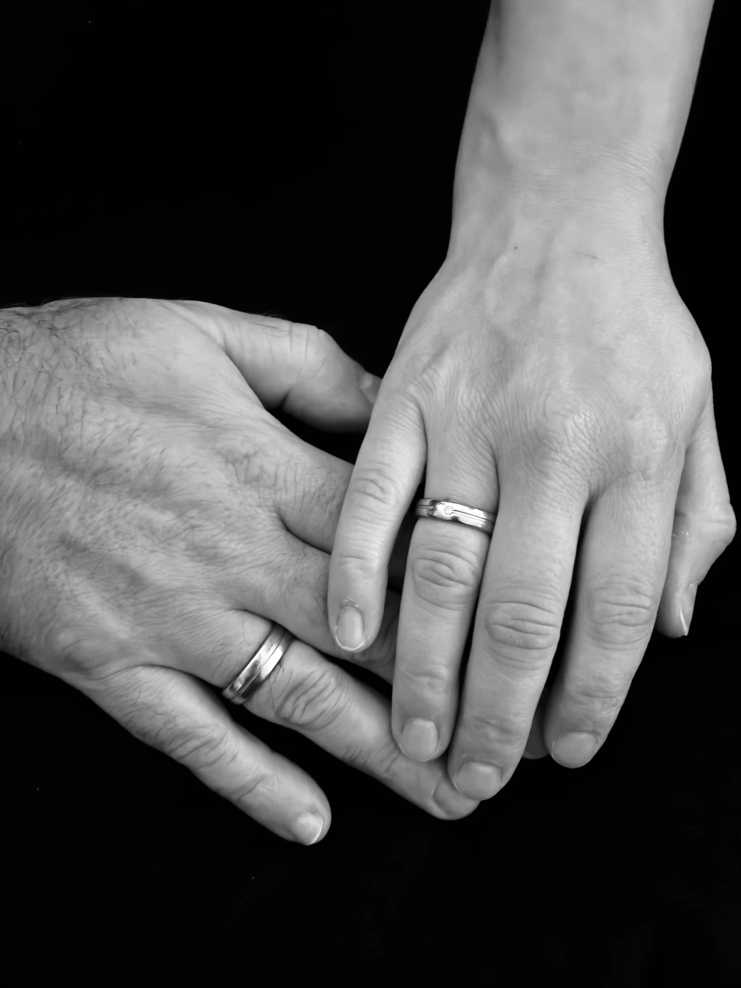 Two pairs of hands resting over one another, photographed close in low light