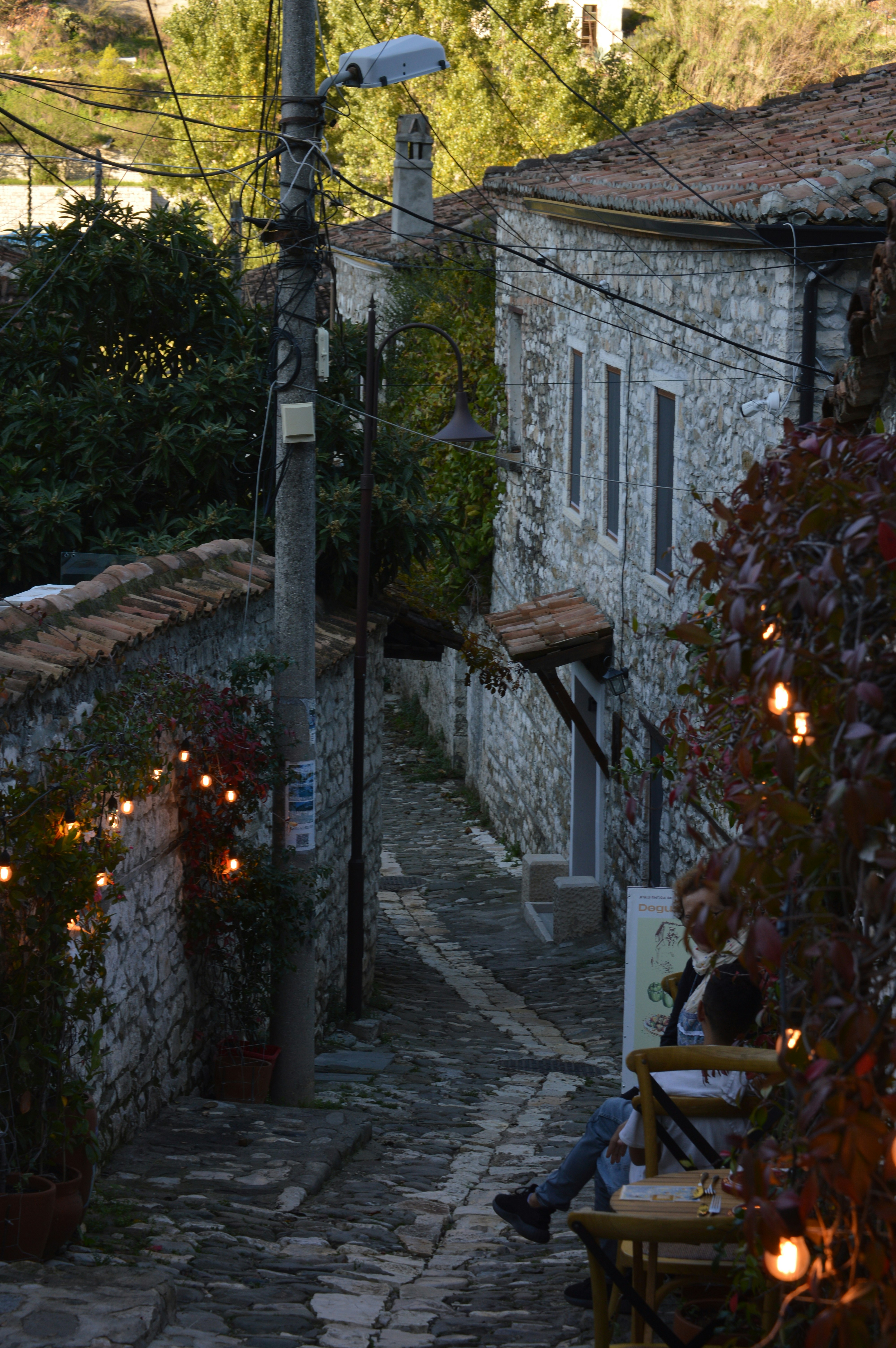 Person sitting on bench in narrow cobblestone alley.