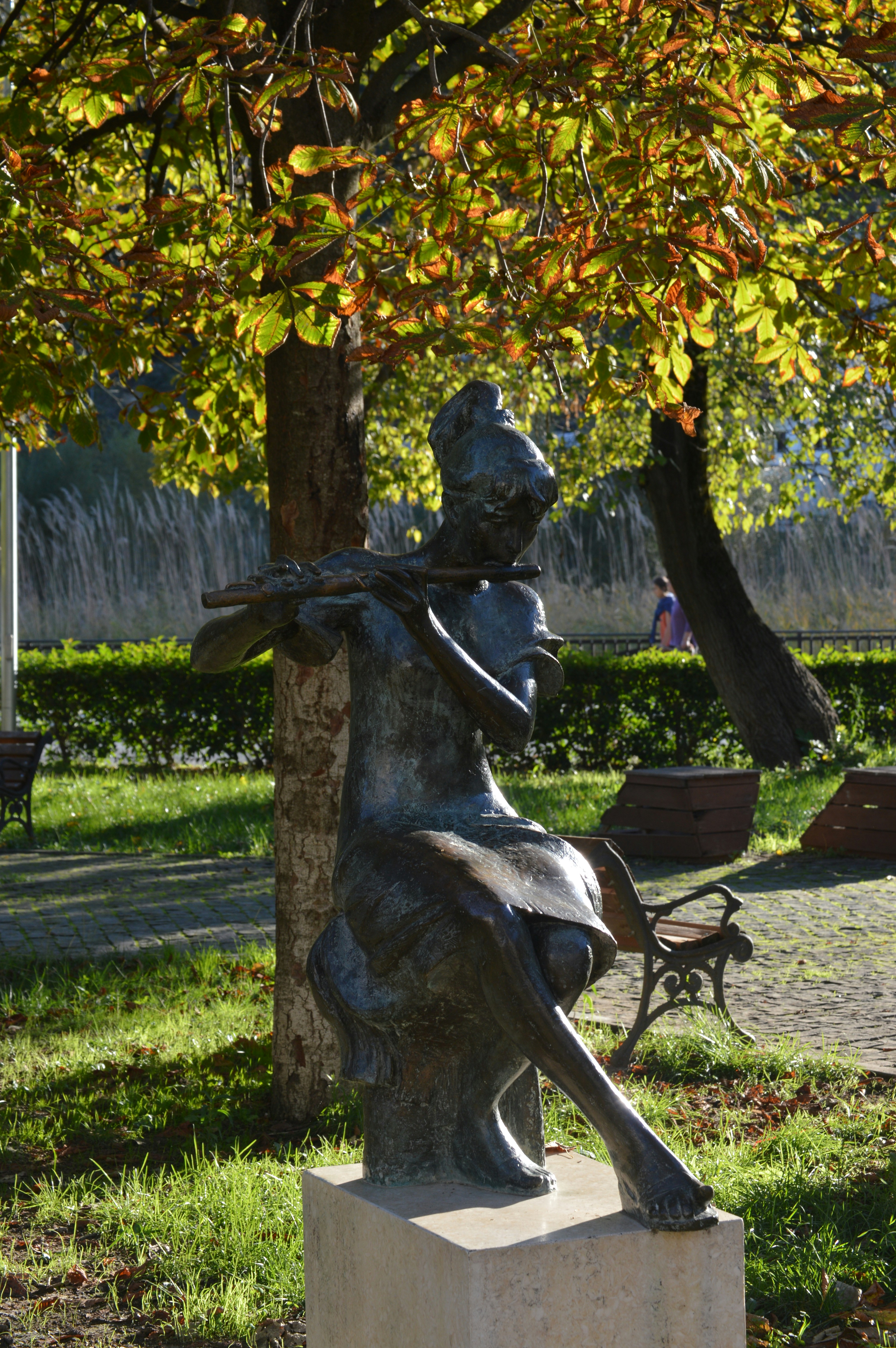 Bronze statue of a woman playing a flute outdoors.