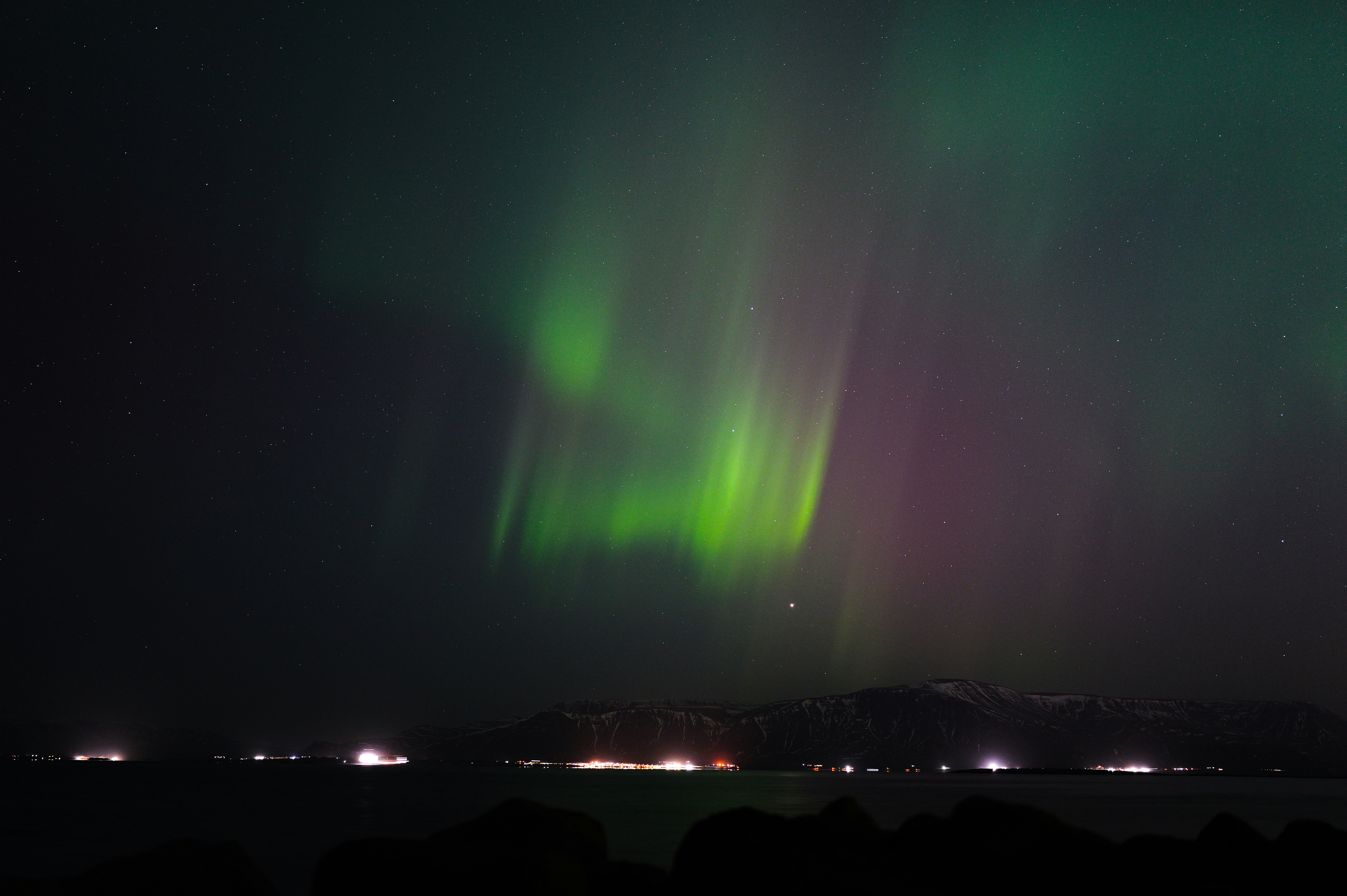 Green and purple aurora borealis over a dark landscape.