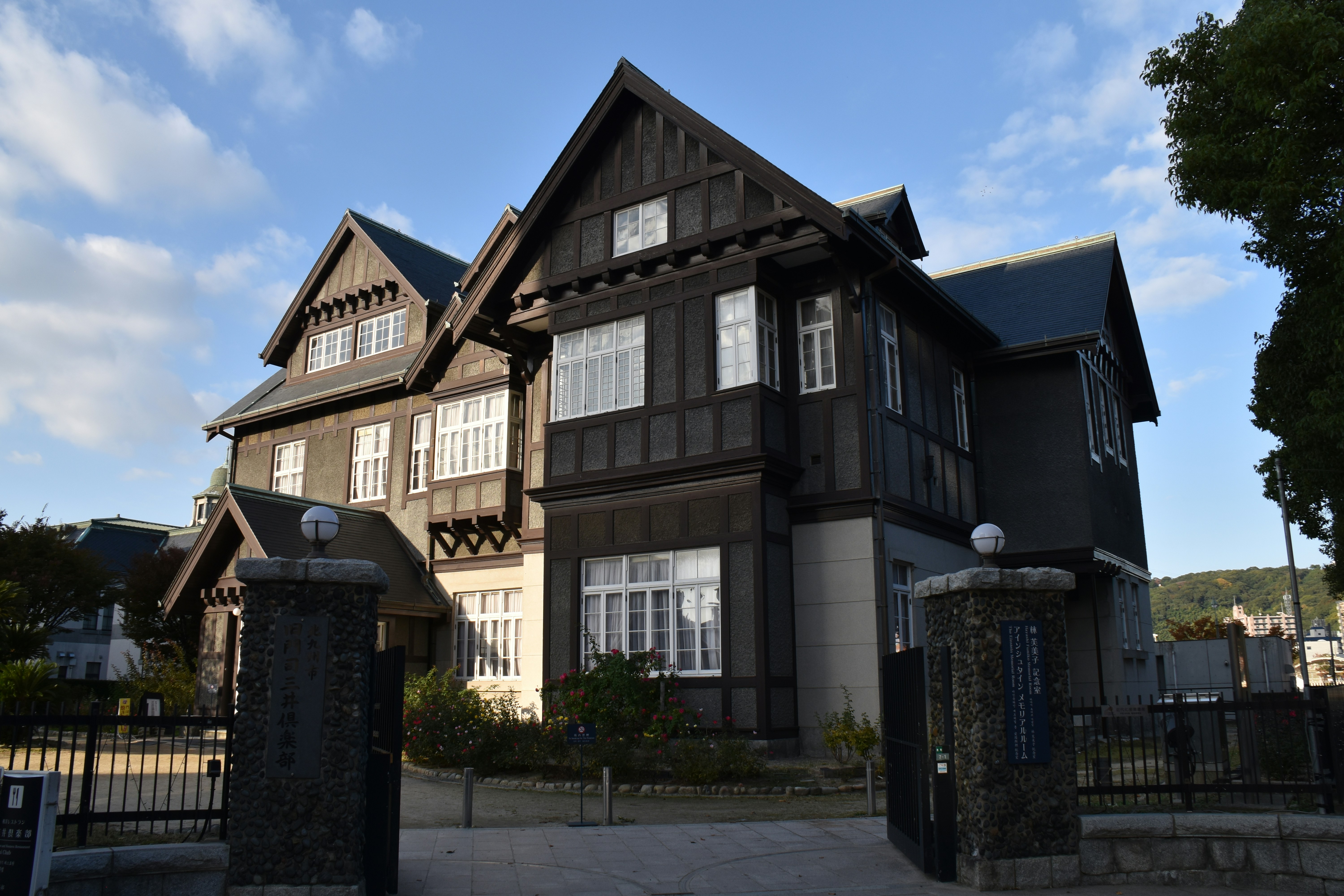 Casa de madeira escura com janelas brancas e pilares de pedra.