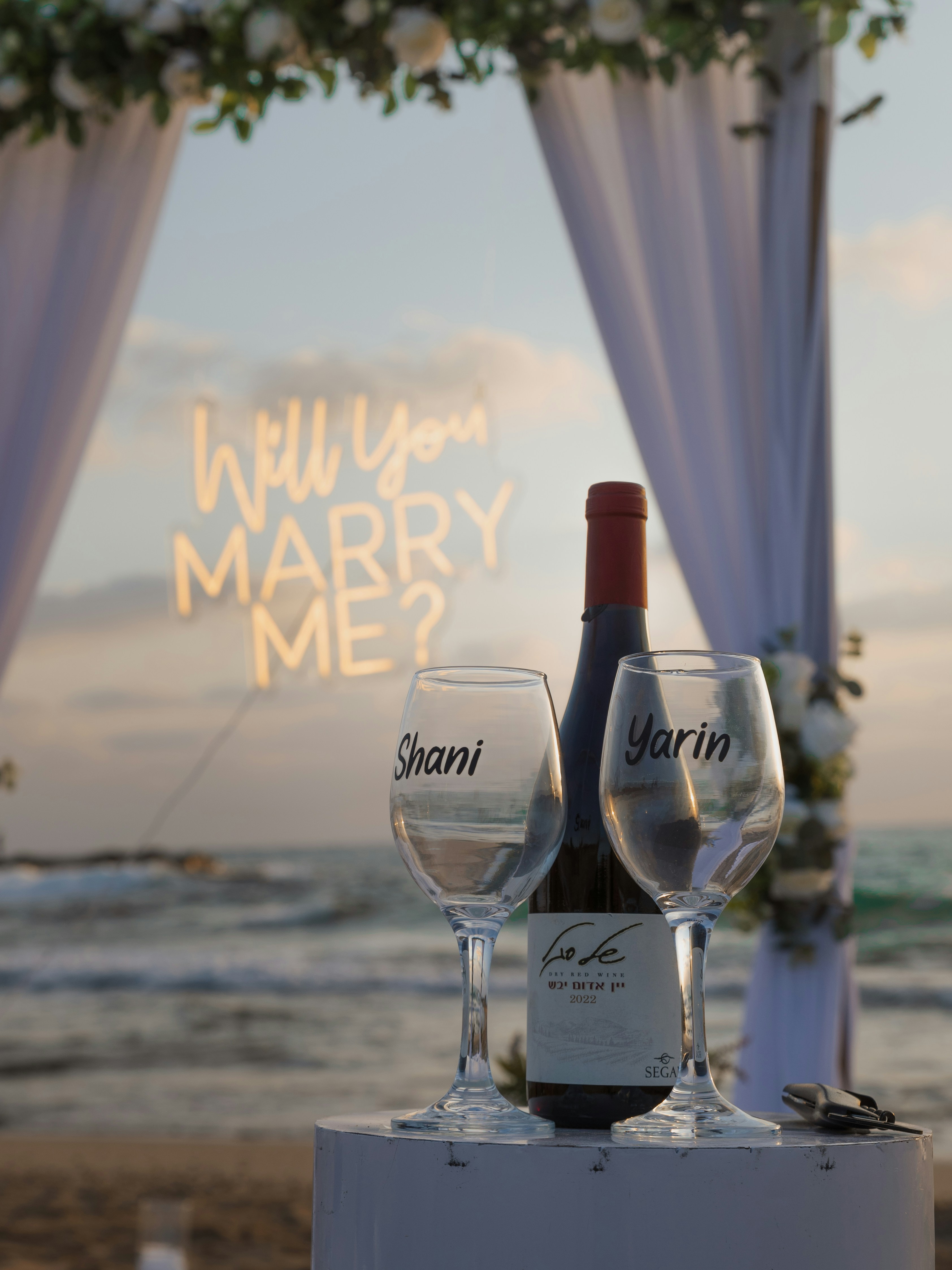 Marriage proposal setup with wine and glasses on beach.
