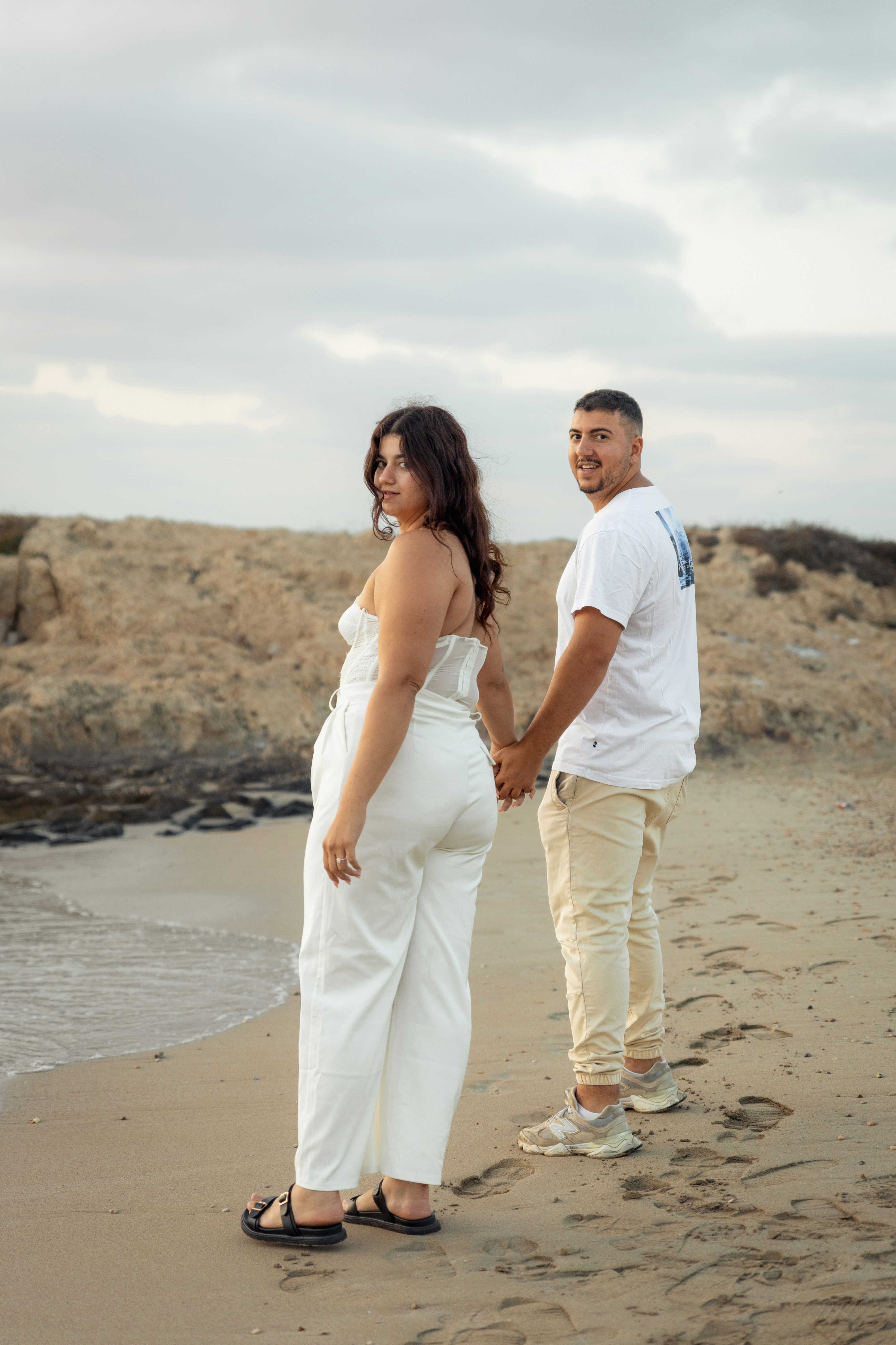 Couple holding hands on a sandy beach.