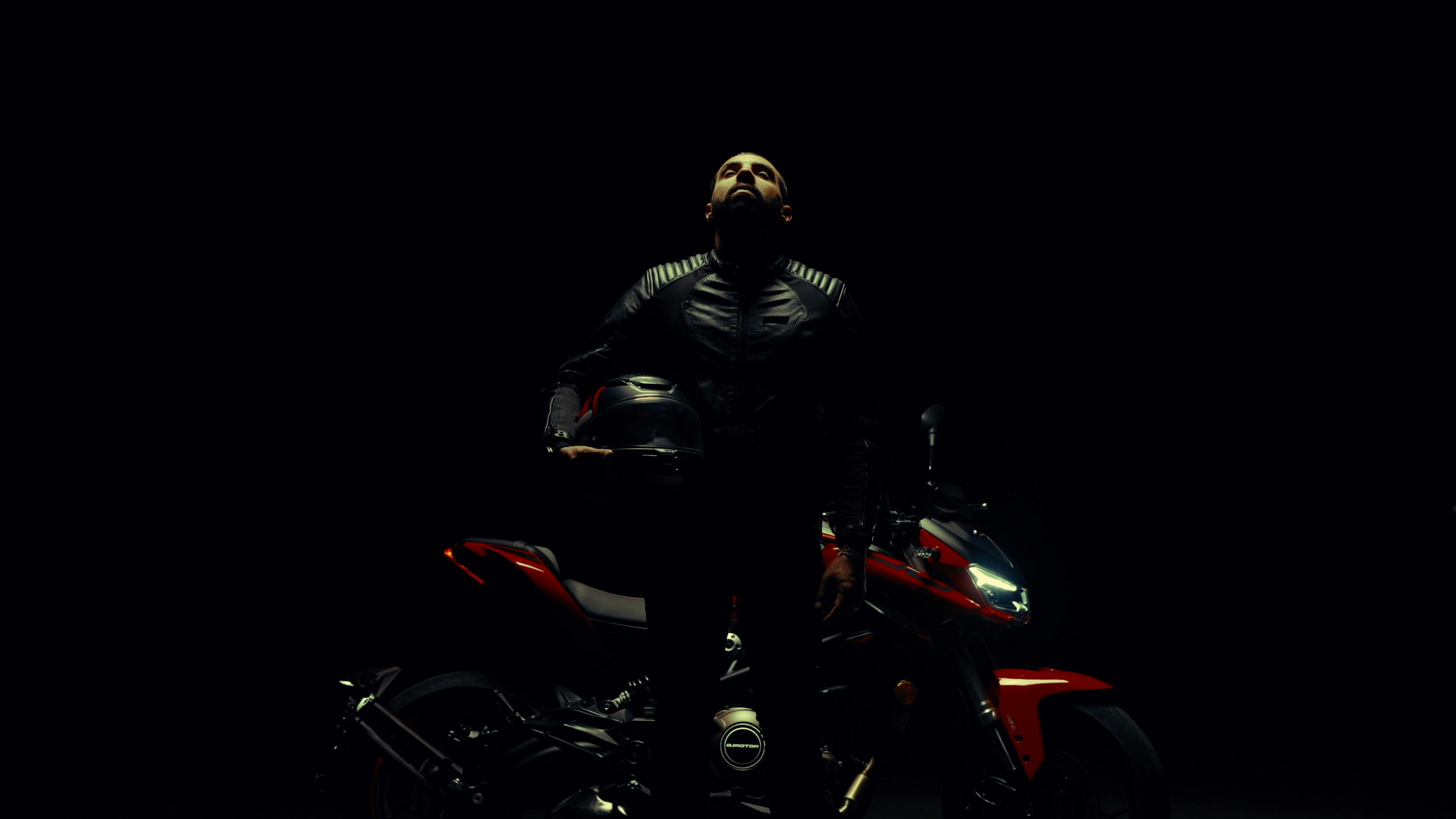 Man holding helmet beside motorcycle in darkness