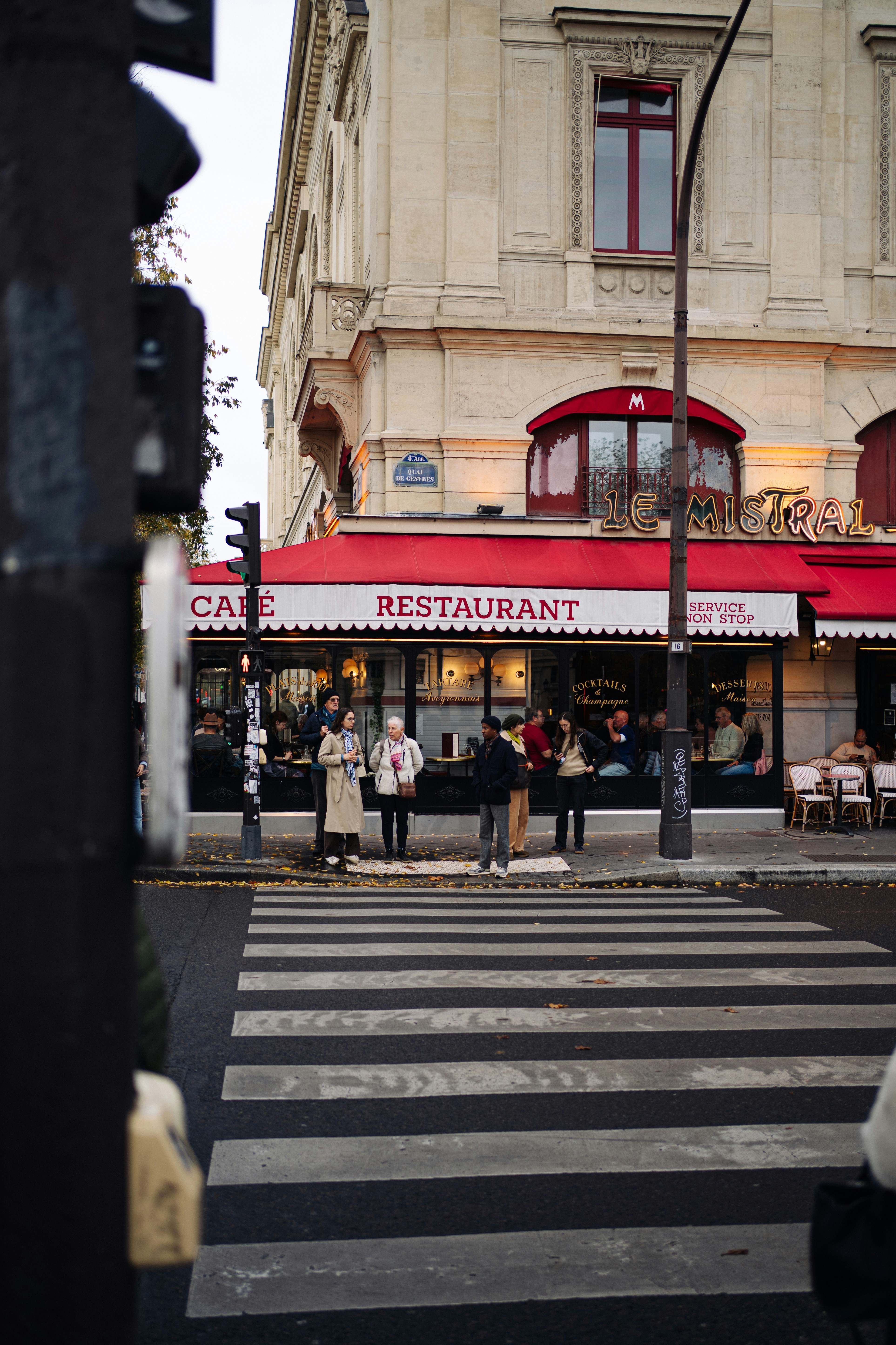 People wait at a crosswalk outside a cafe restaurant.