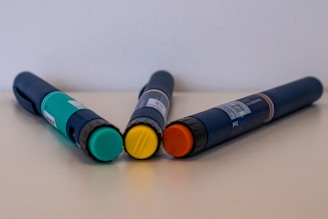 Three injection pens with colored caps on table.