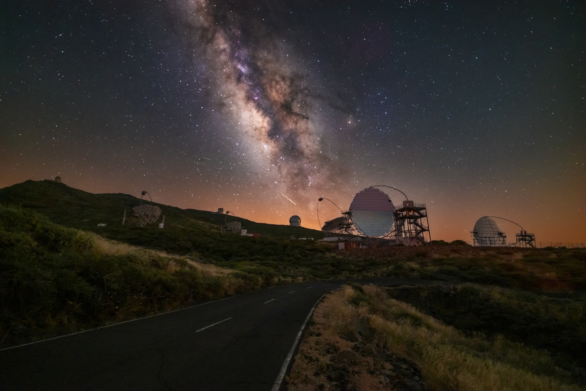 The Milky Way above the observatory domes at Roque de los Muchachos, with a mountain road curving in the foreground