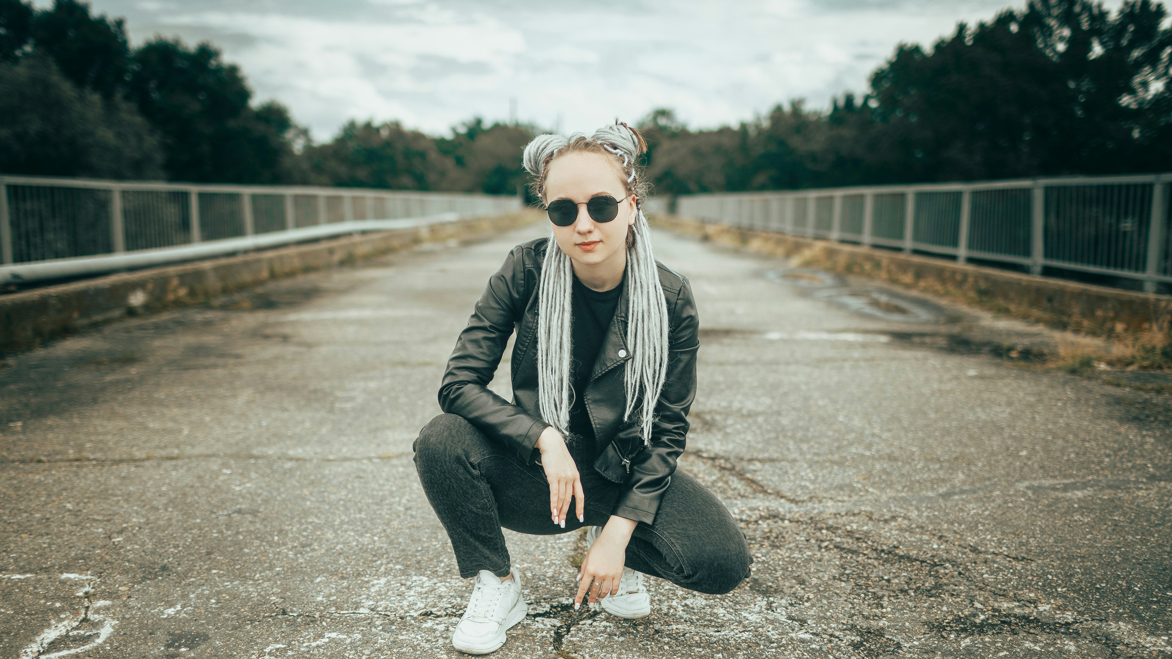 Woman in sunglasses crouching on a road.