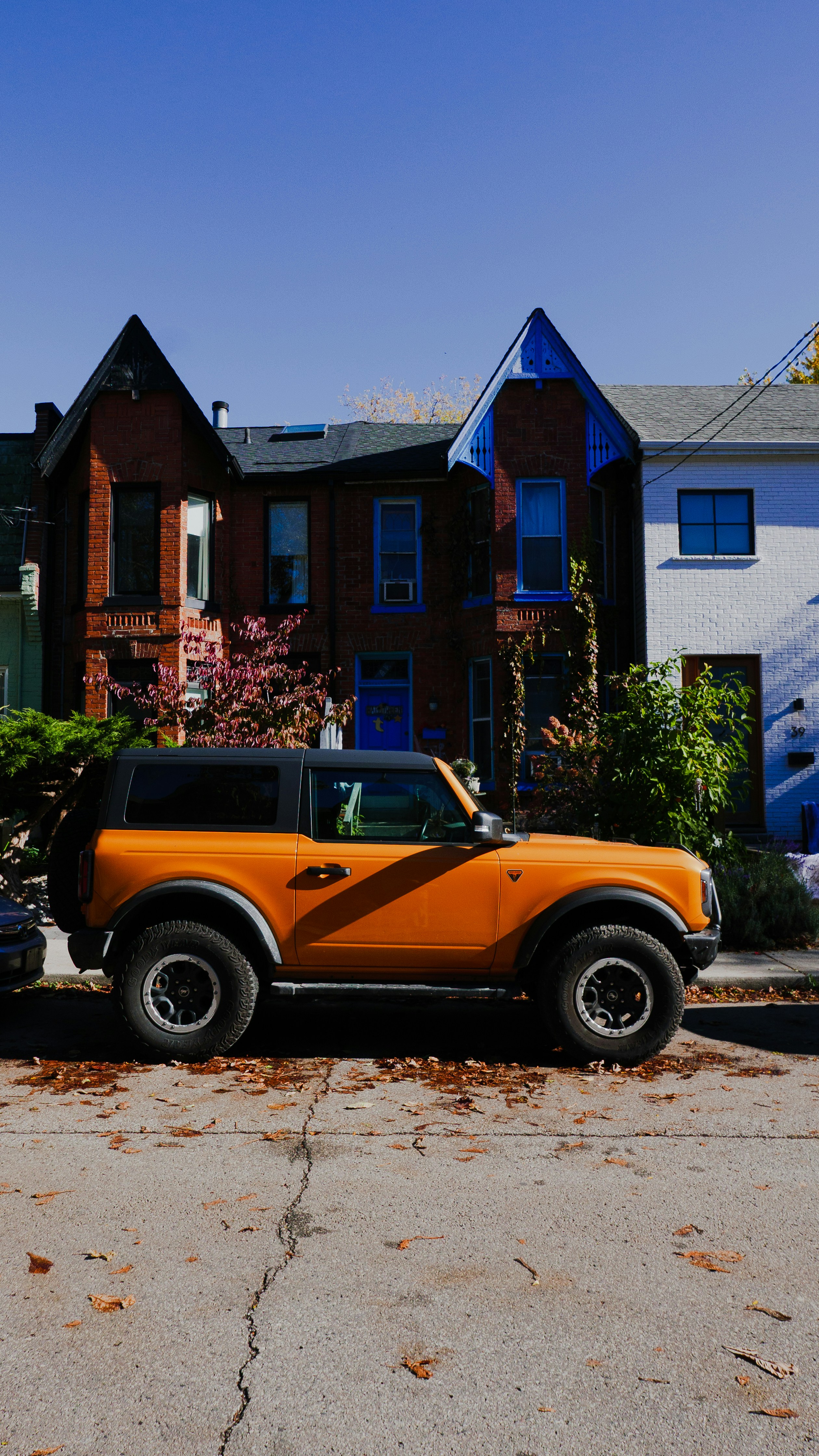Ford bronco naranja estacionado en la calle con casas detrás