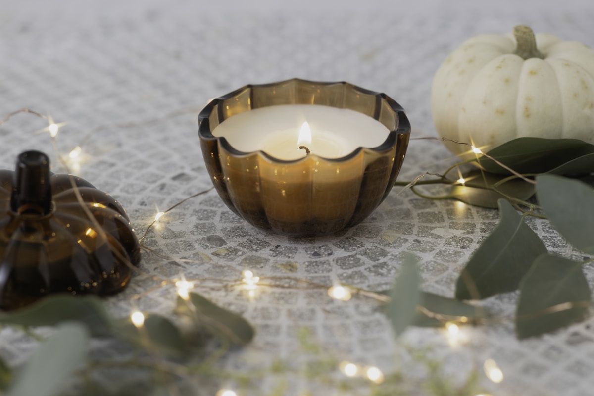 Fall candle in amber glass holder surrounded by mini pumpkins and fairy lights
