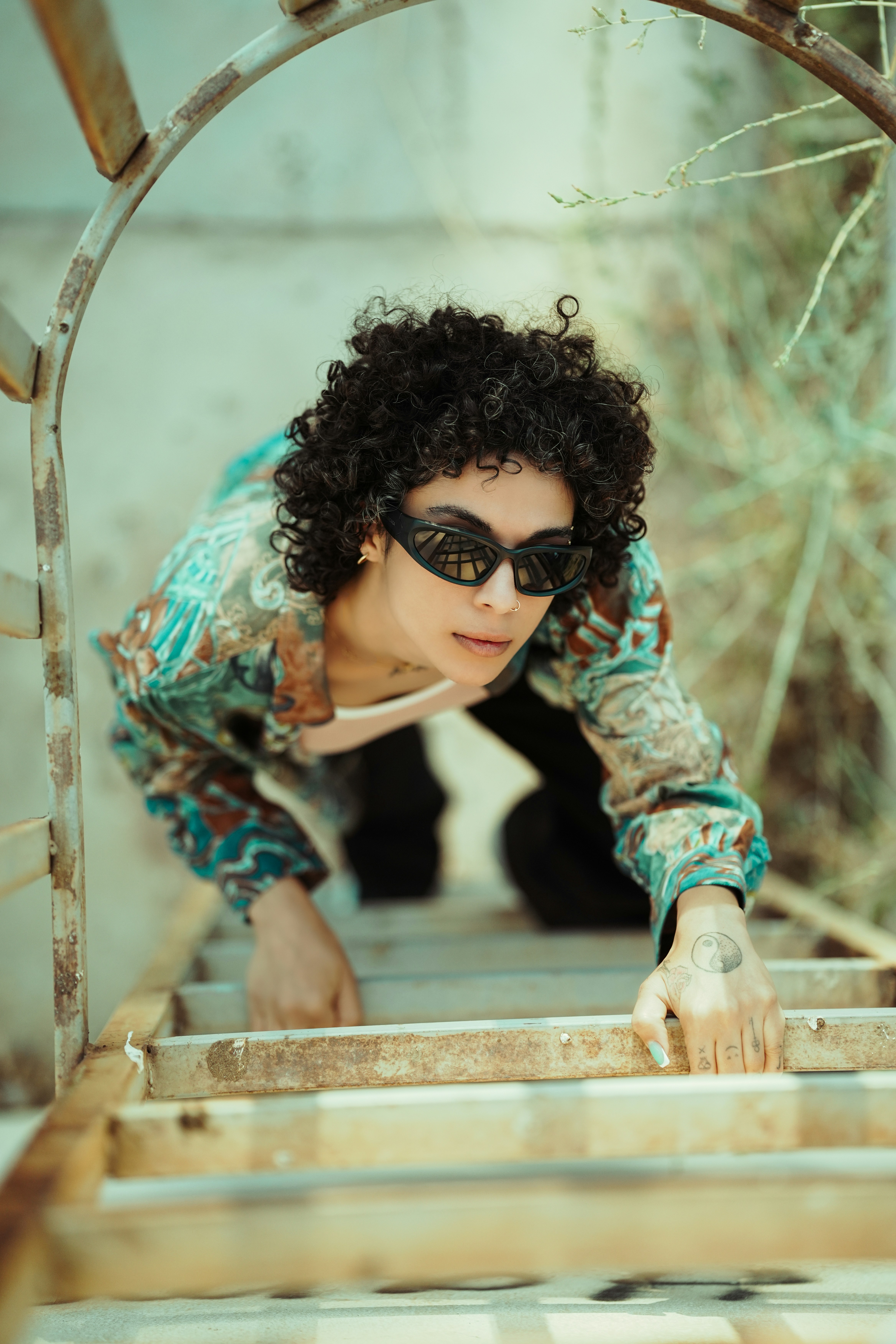 Woman with curly hair wearing sunglasses climbs ladder