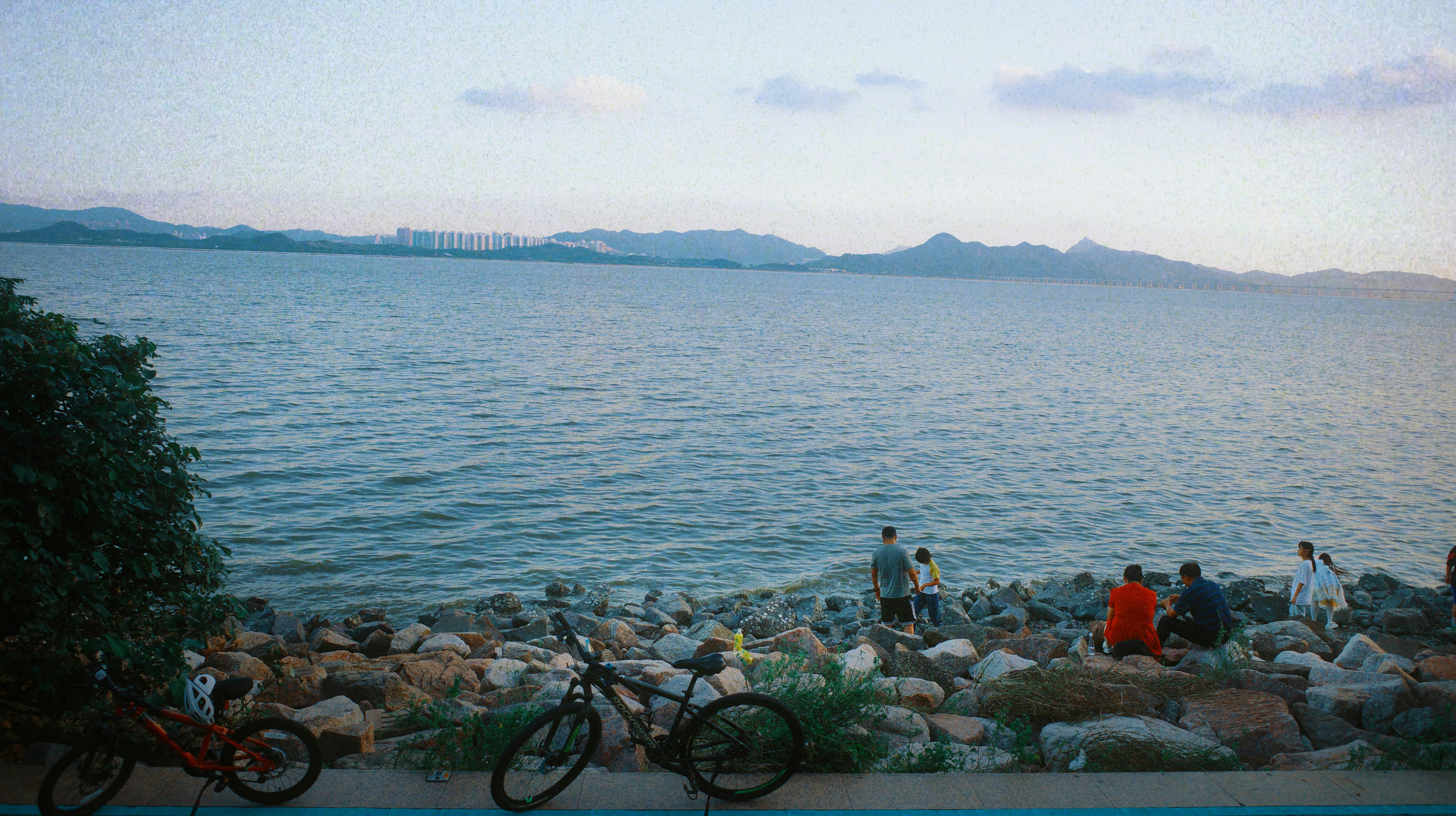 People gathered by a rocky shore with bicycles.