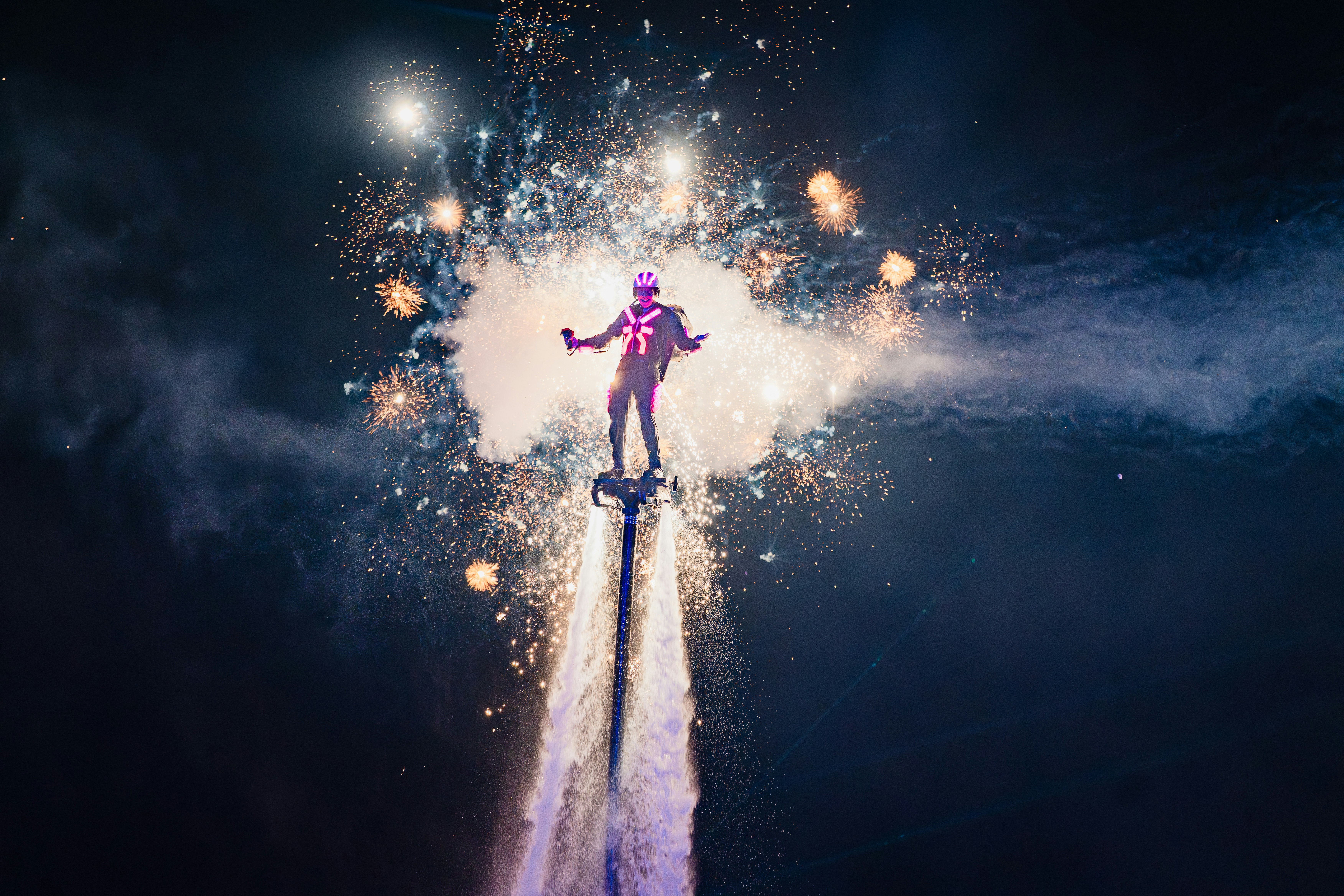 Performer on jetpack with fireworks in the night sky