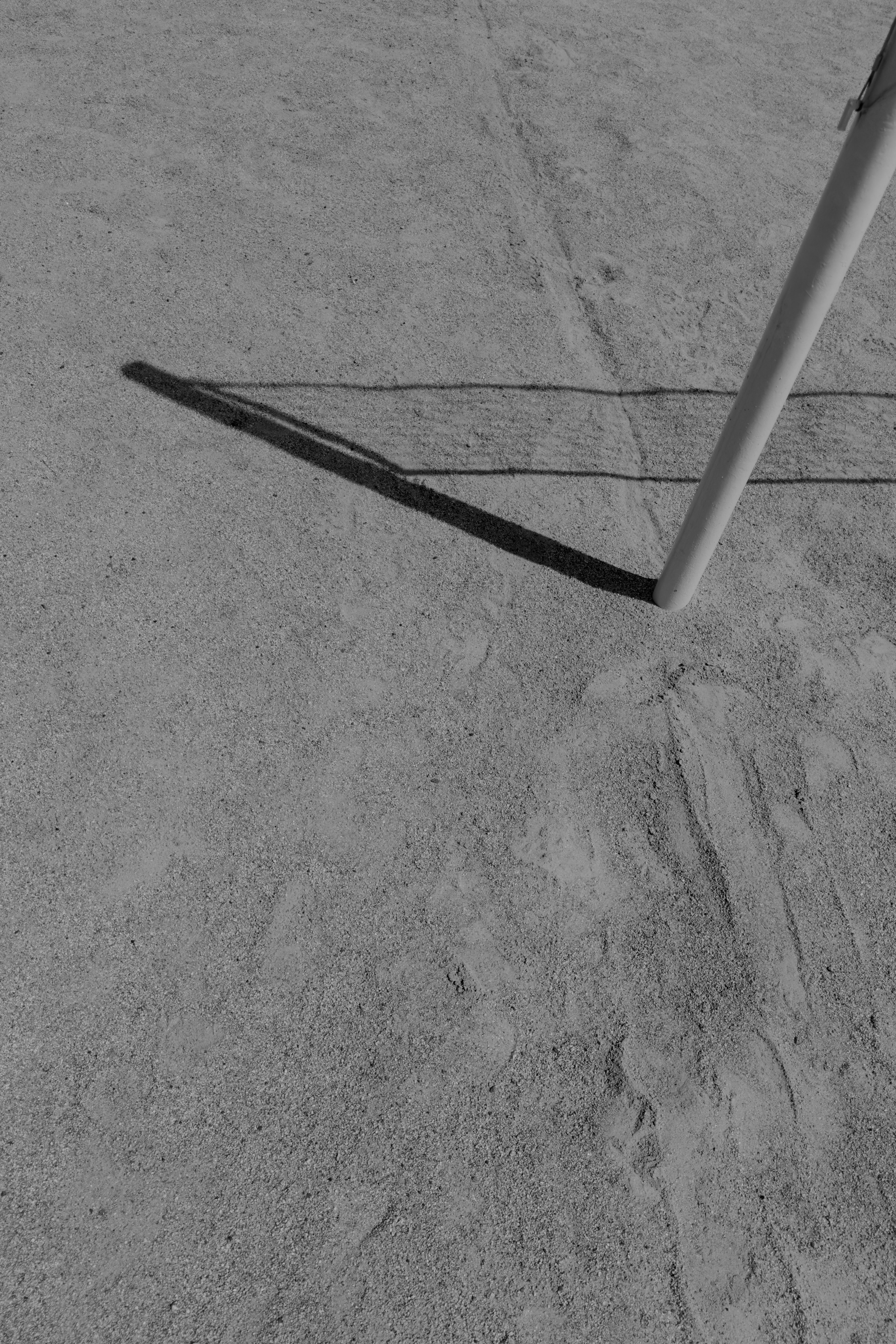 A pole casts a long shadow on sandy ground.