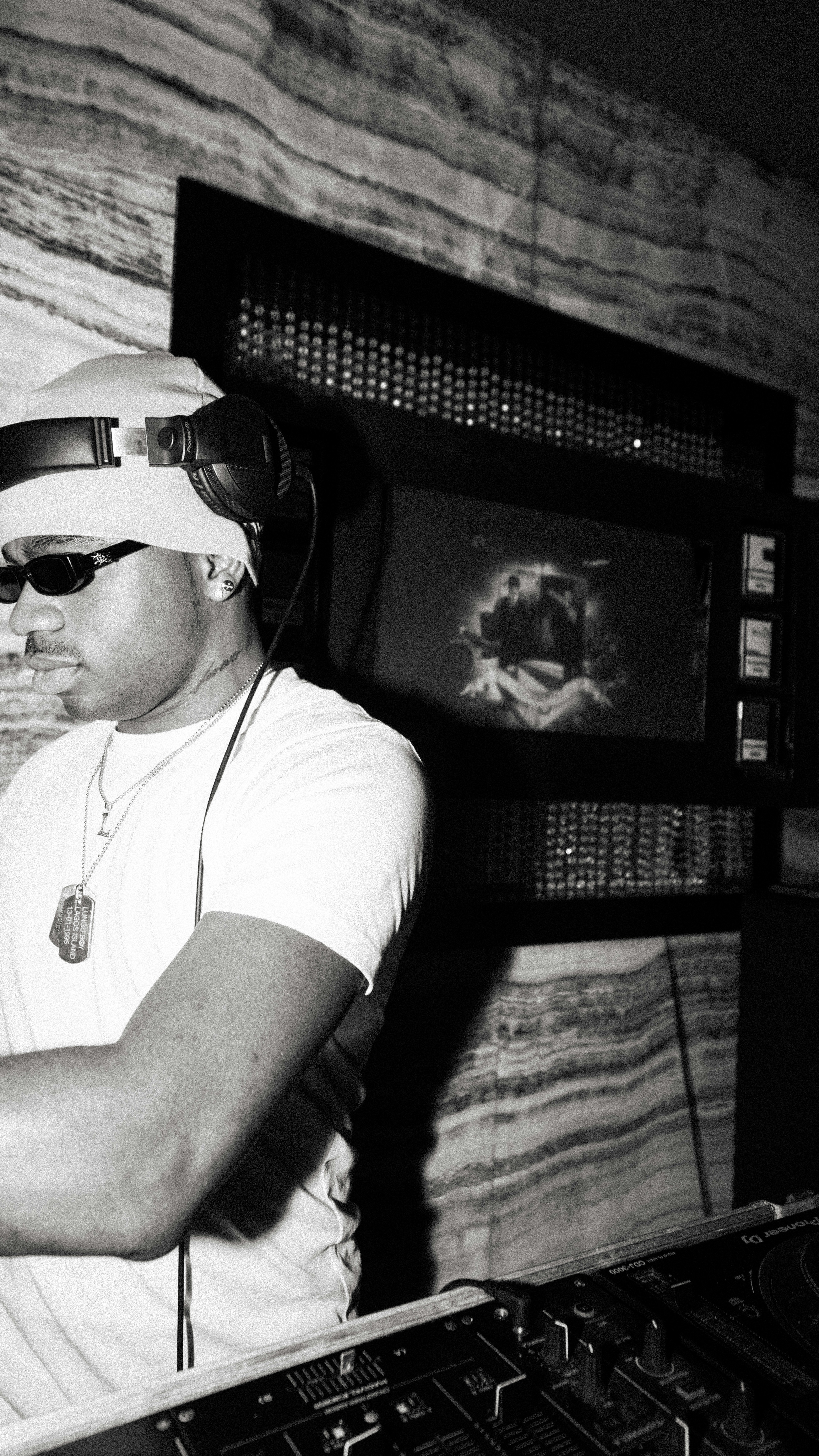 Dj wearing headphones and sunglasses at a console.