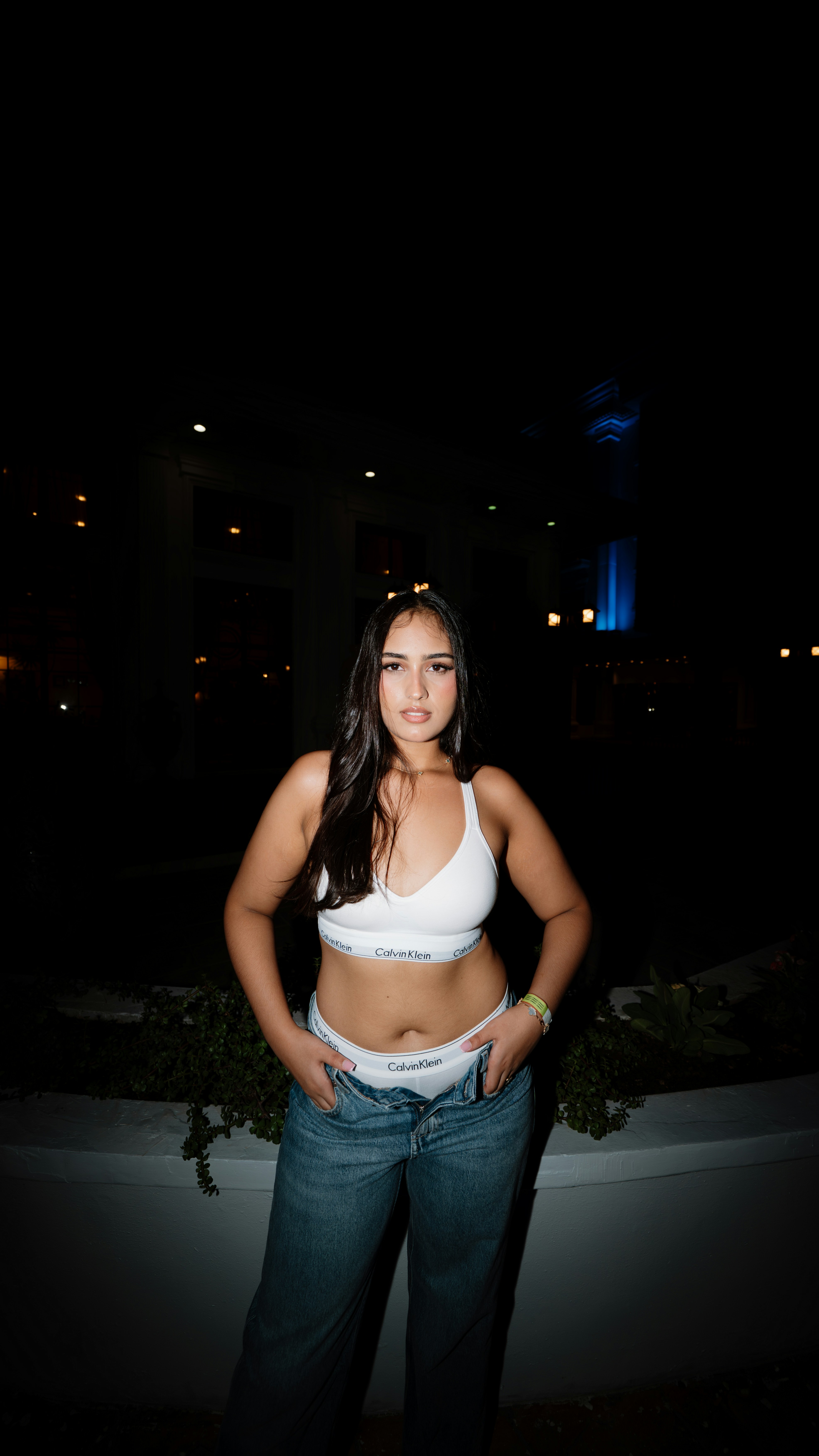 Uma jovem de jeans e sutiã branco à noite.