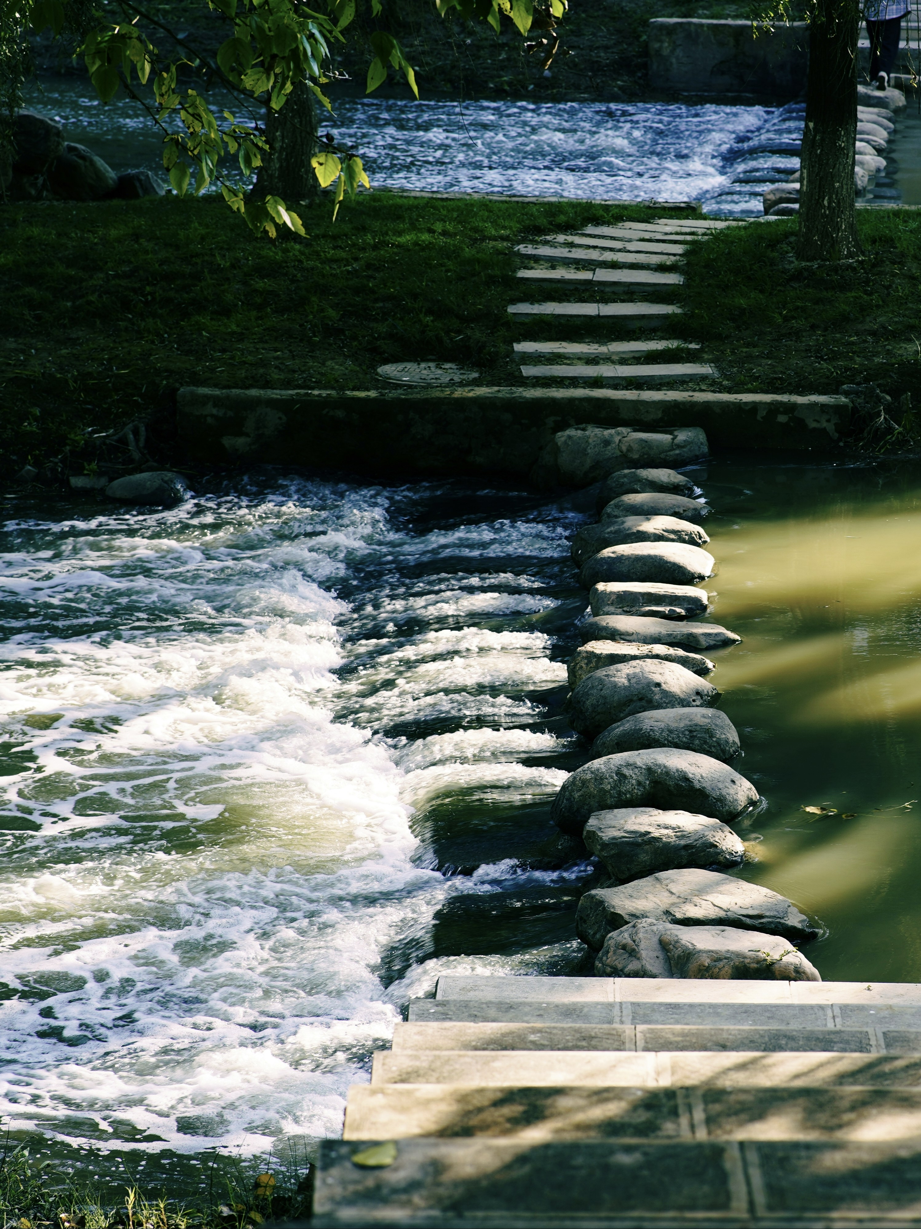 Stepping stones cross a flowing river in a park.