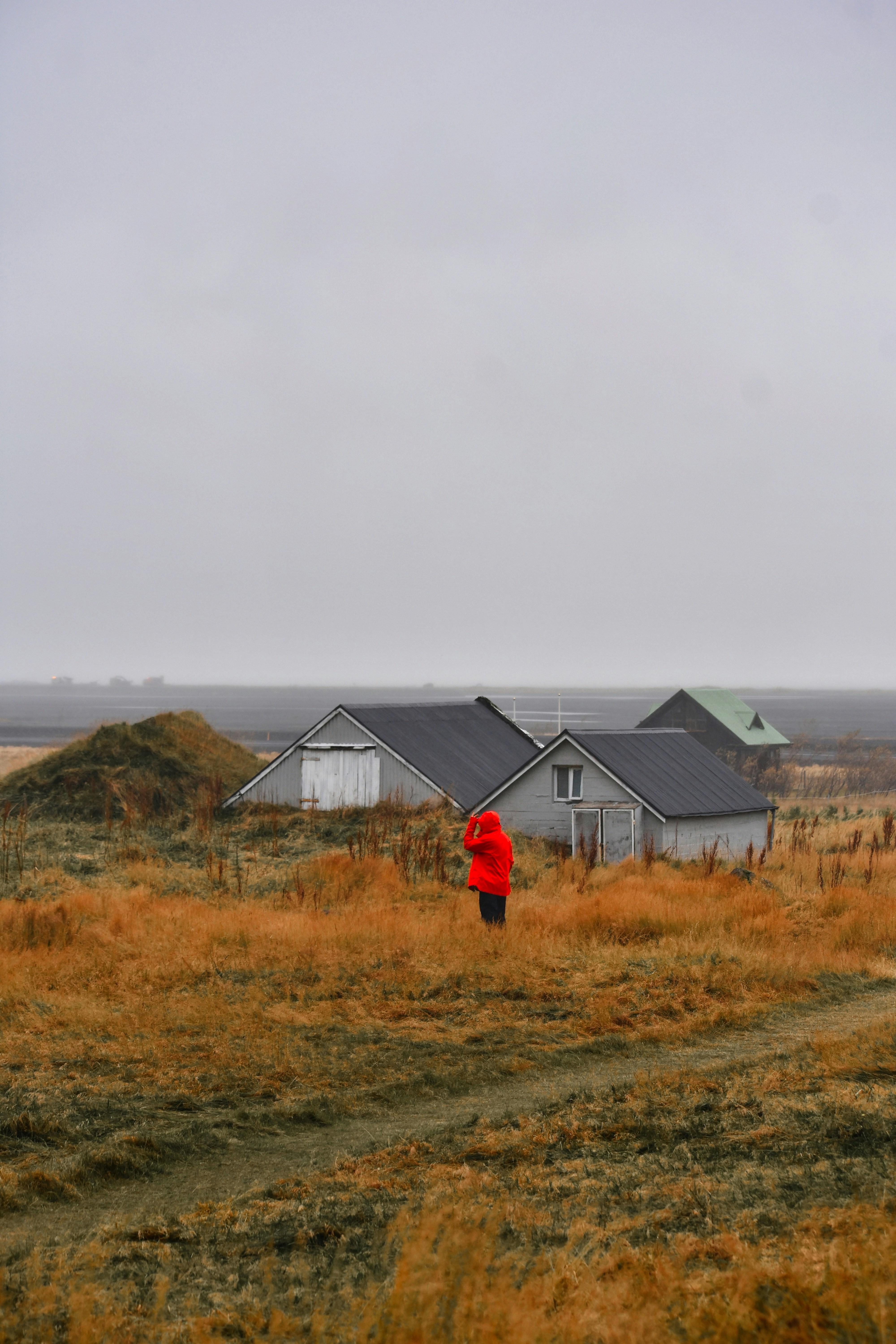Person in roter Jacke nahe ländlichen Gebäuden bei bewölktem Wetter