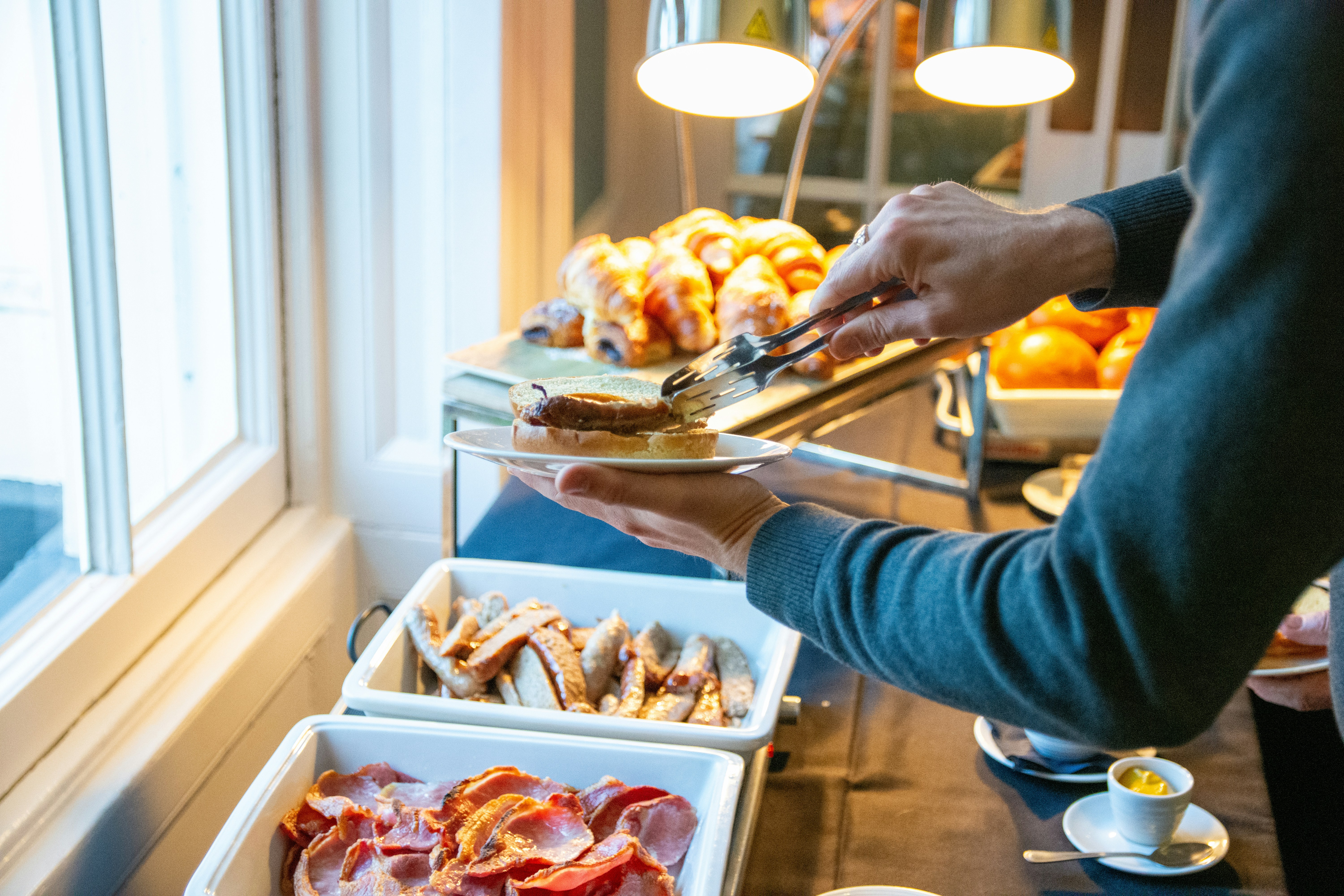 Person serving breakfast buffet with bacon and pastries