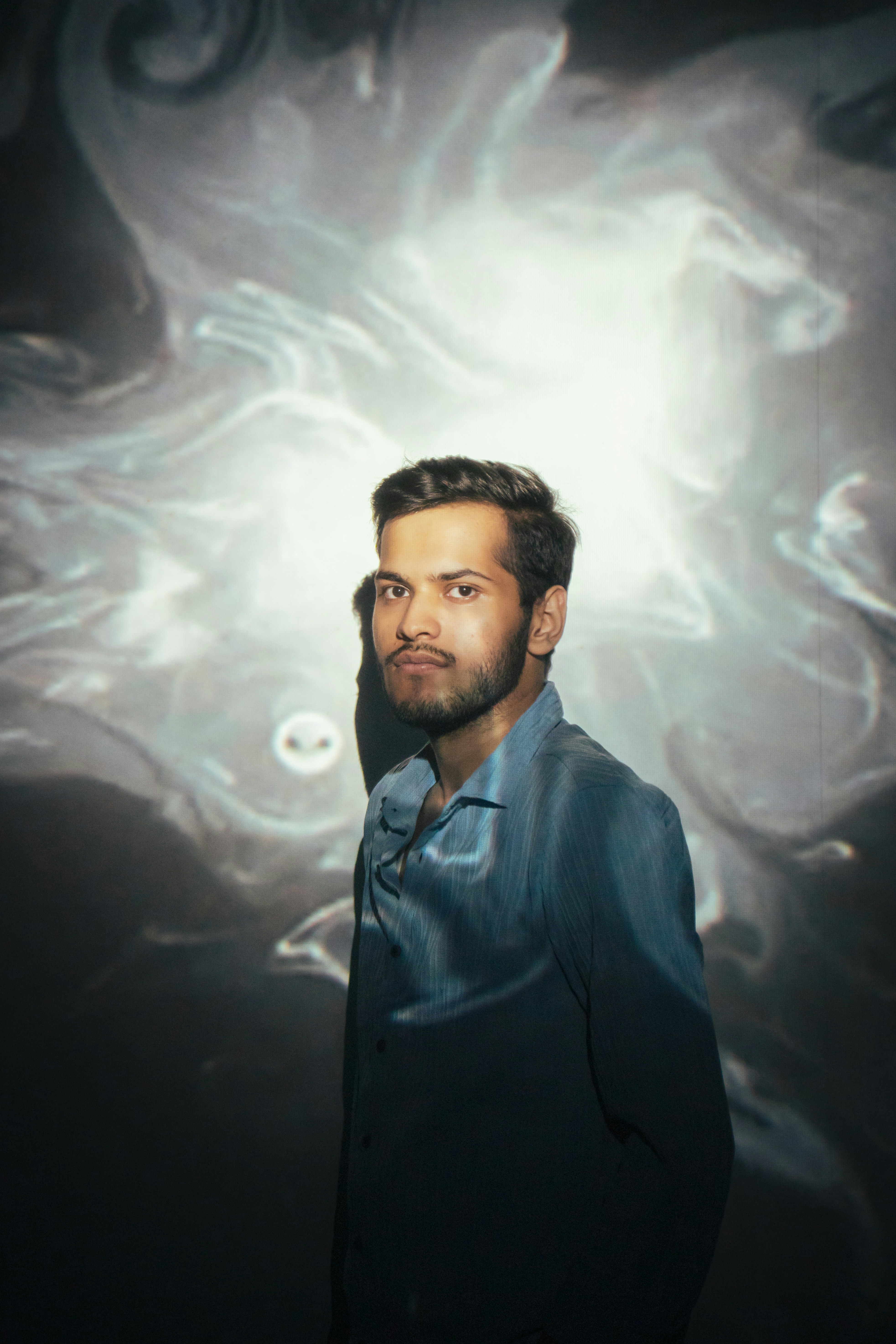 Mann mit Bart und blauem Hemd vor abstraktem Hintergrund