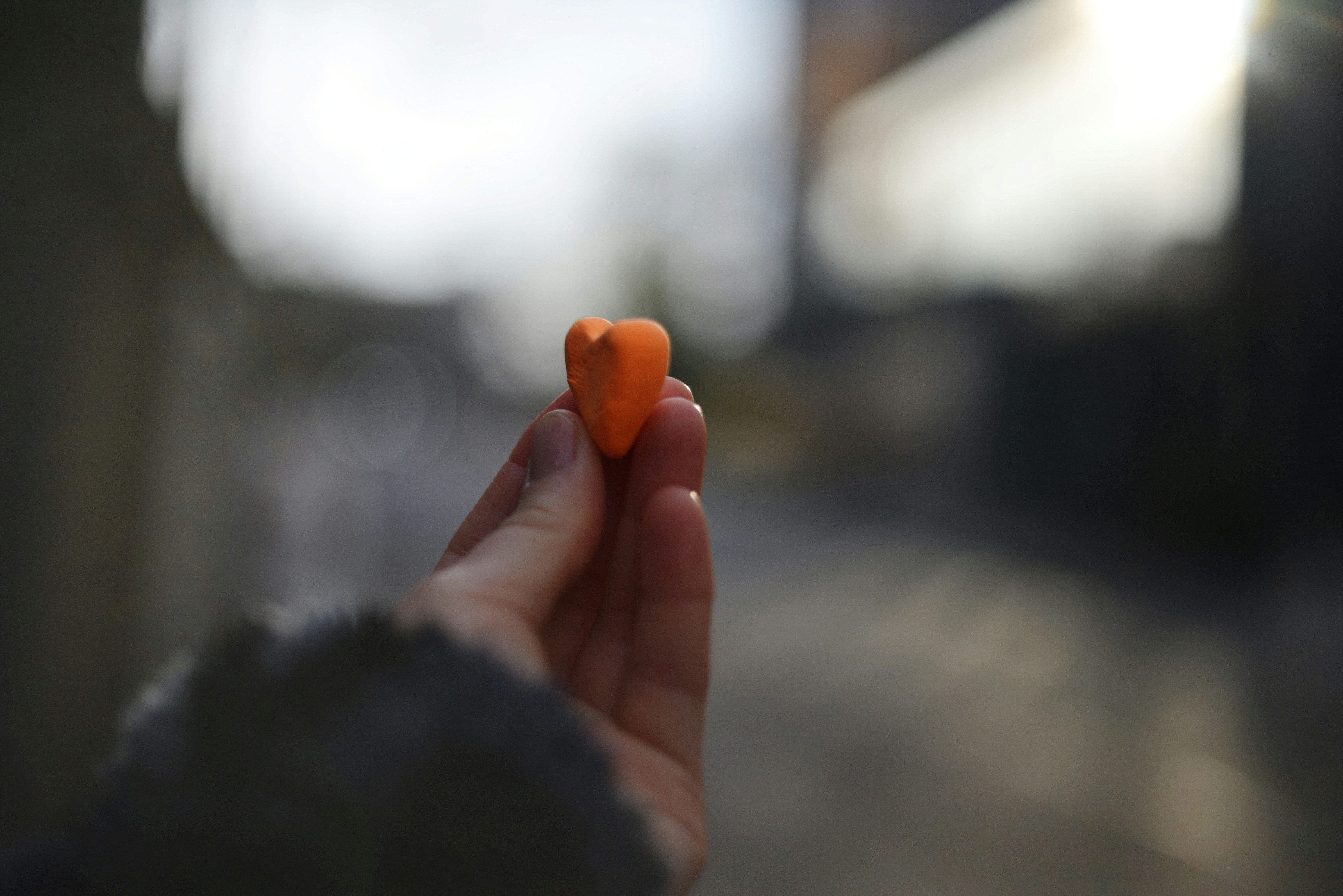 A hand holds a small orange pepper.