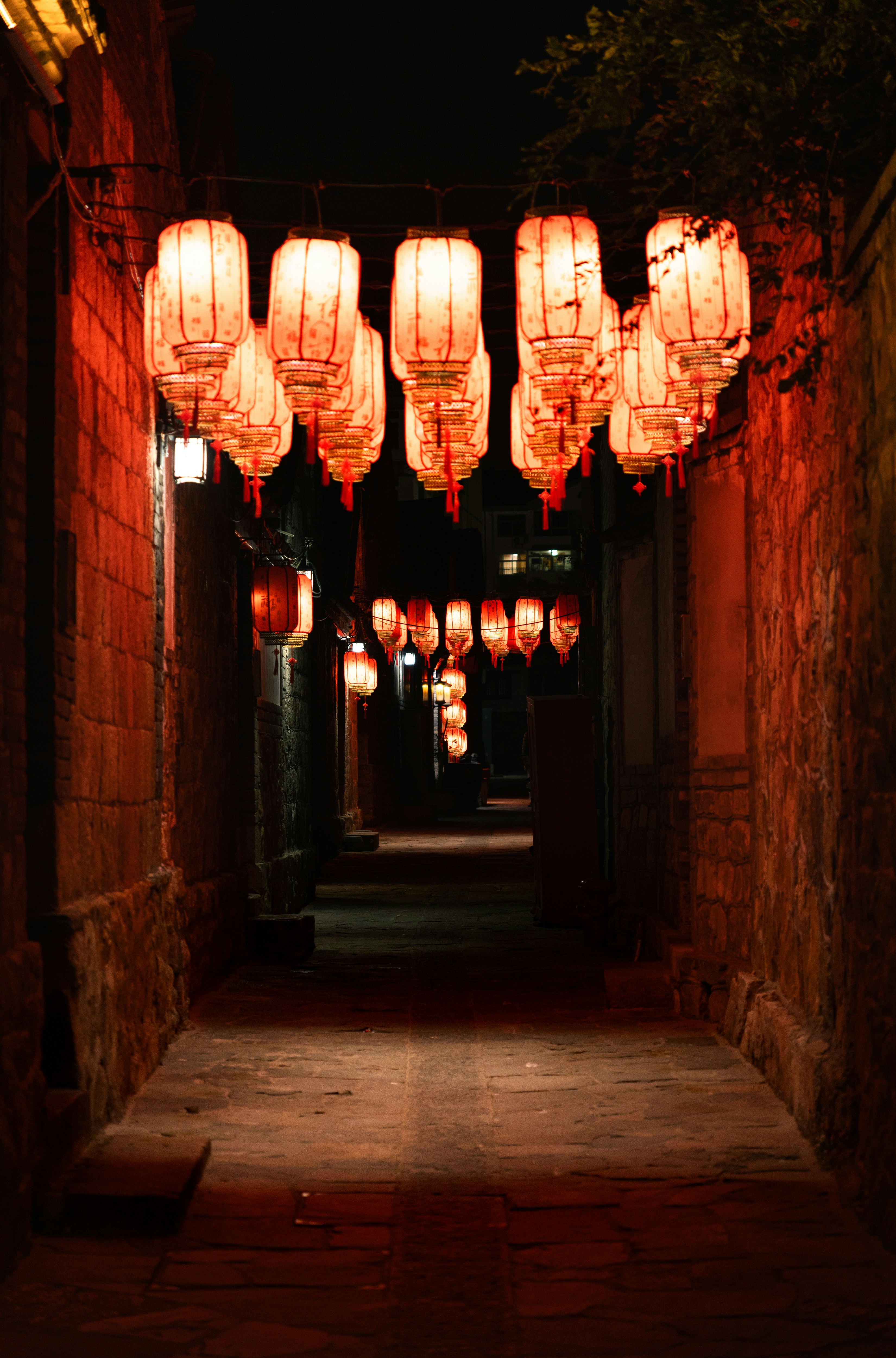 Red lanterns illuminate a narrow alleyway at night.