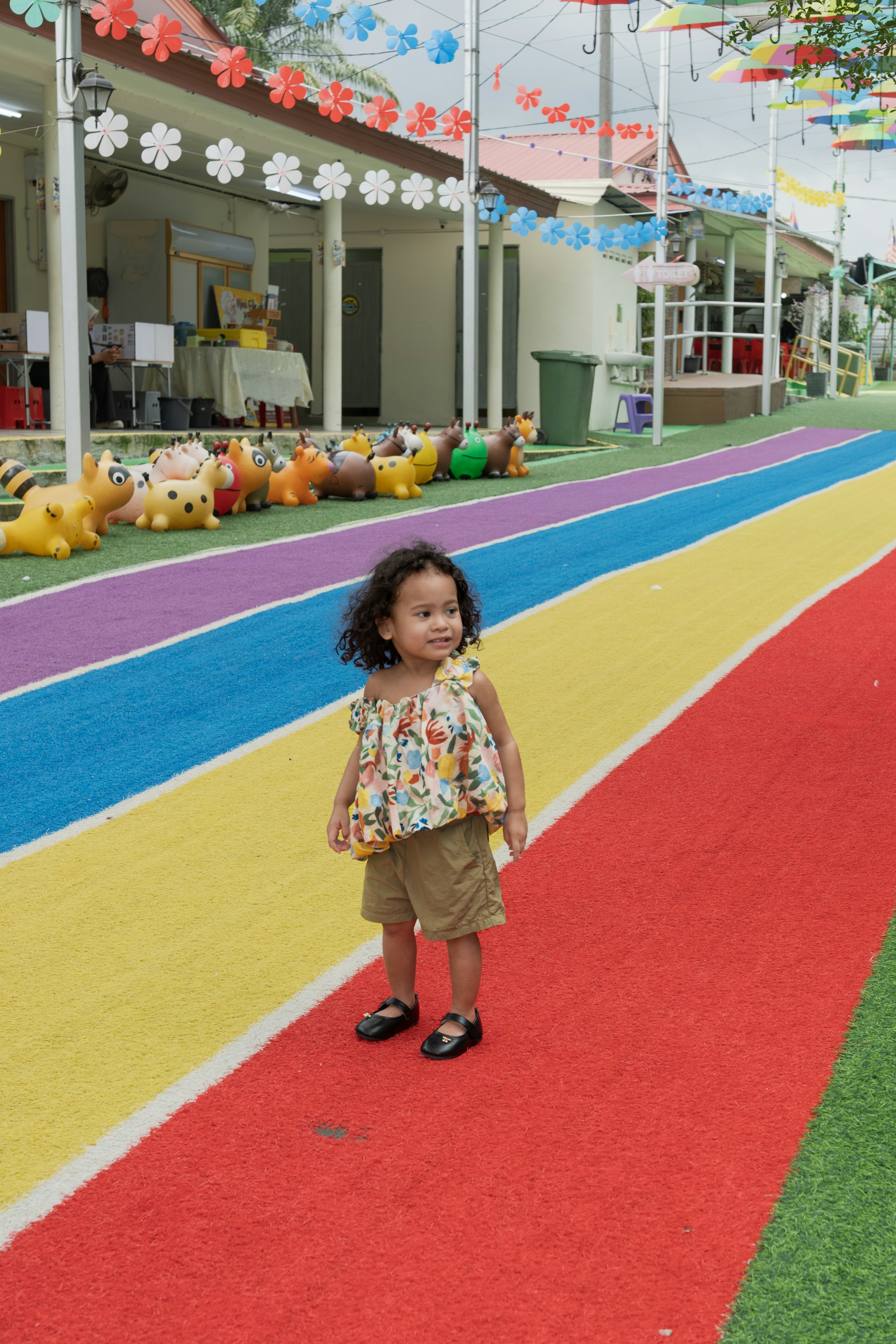 Young child stands on a colorful rainbow path.
