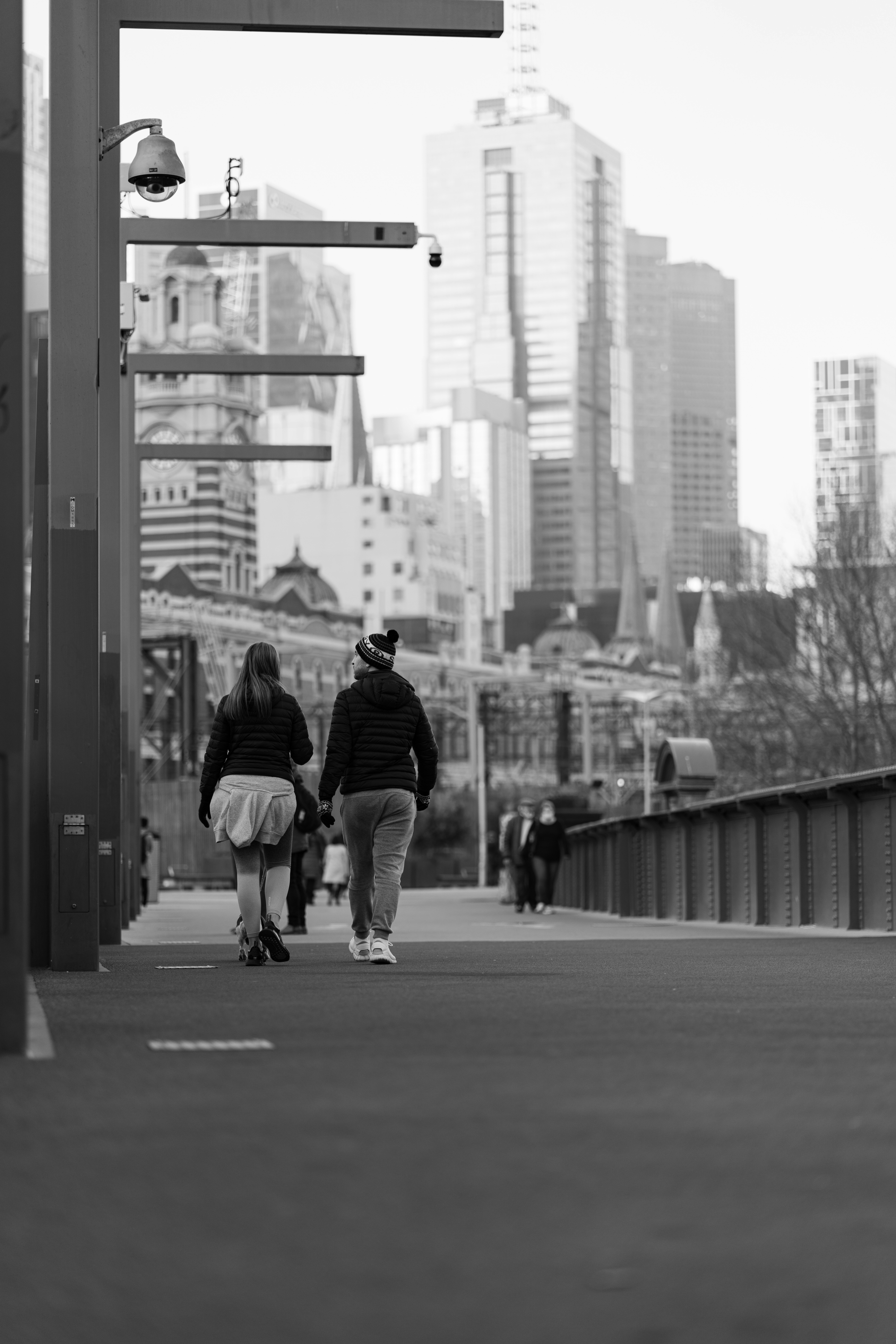 Two people walk on a bridge with city skyline.