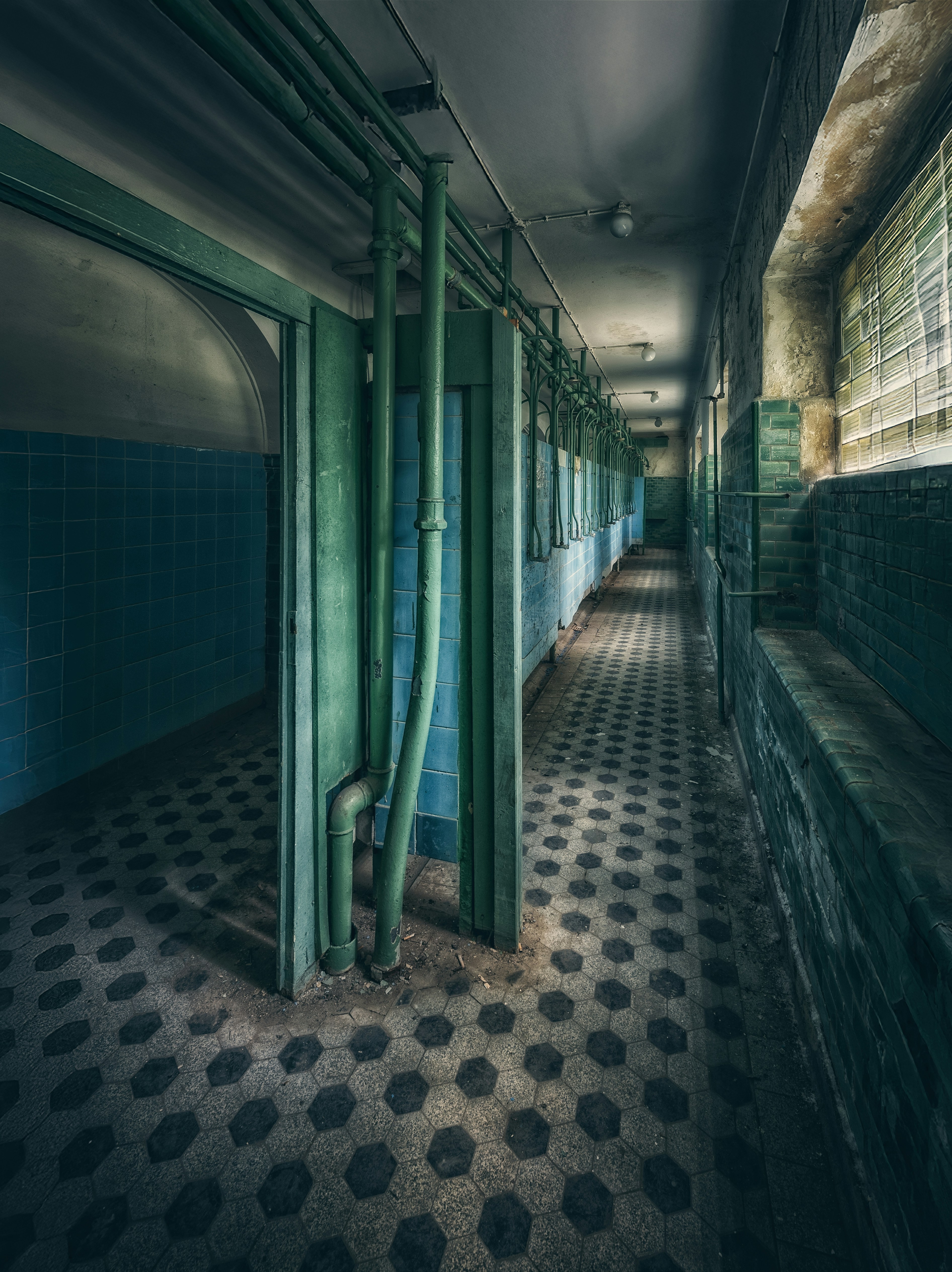 Abandoned hallway with tiled walls and hexagonal floor.