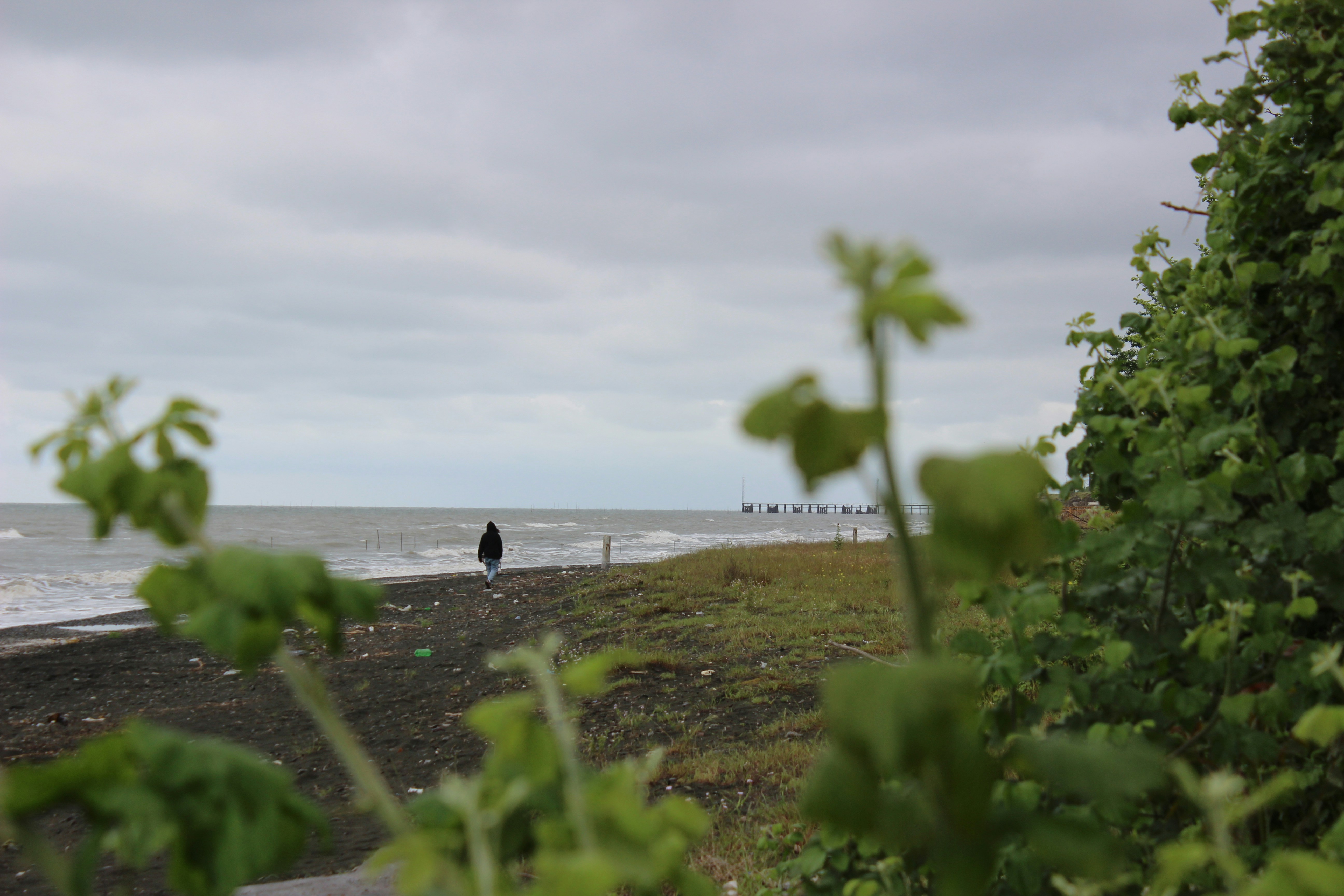 A person walks along a deserted beach under cloudy skies.