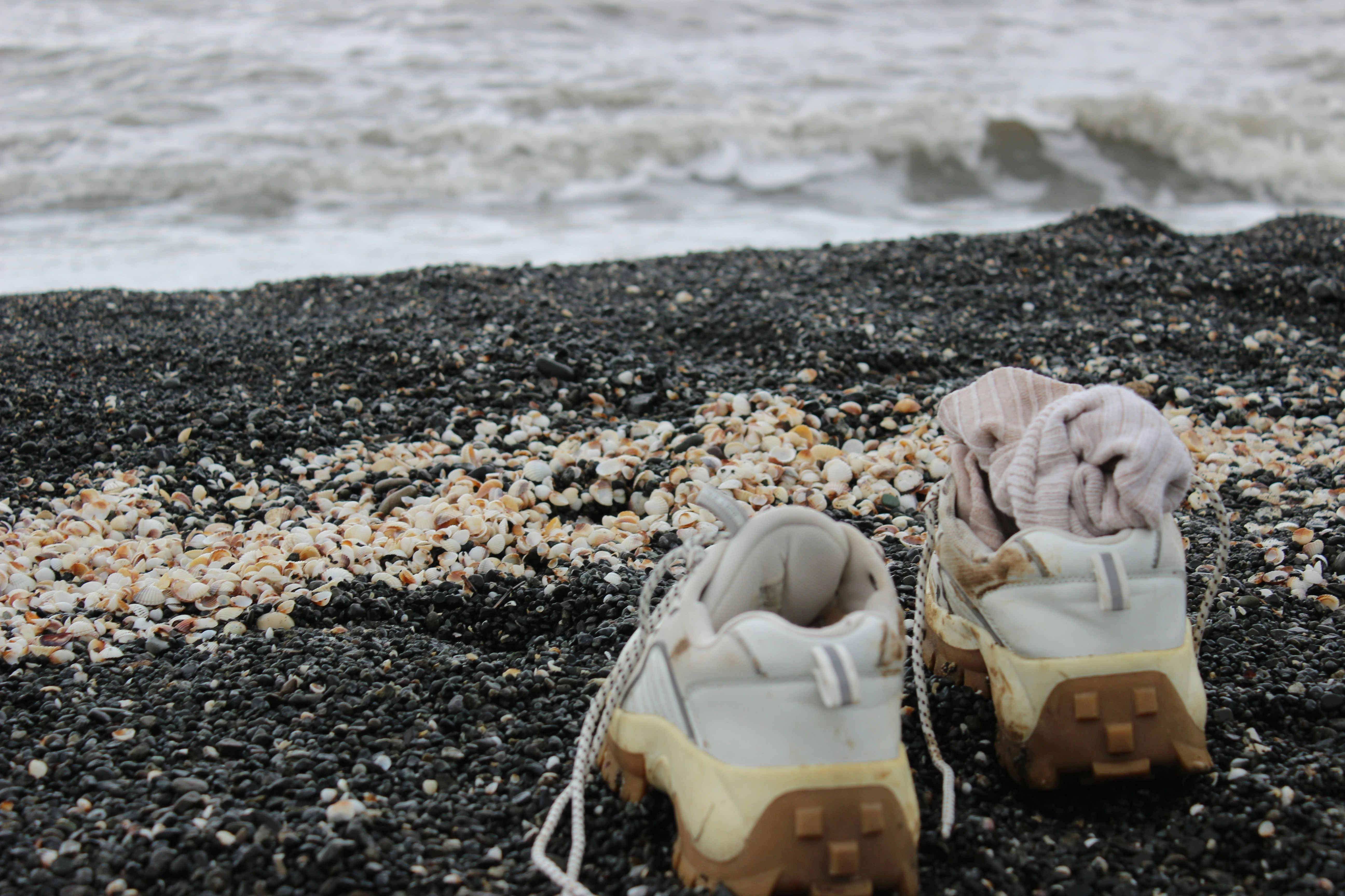 Pair of shoes on a pebble beach with ocean waves.