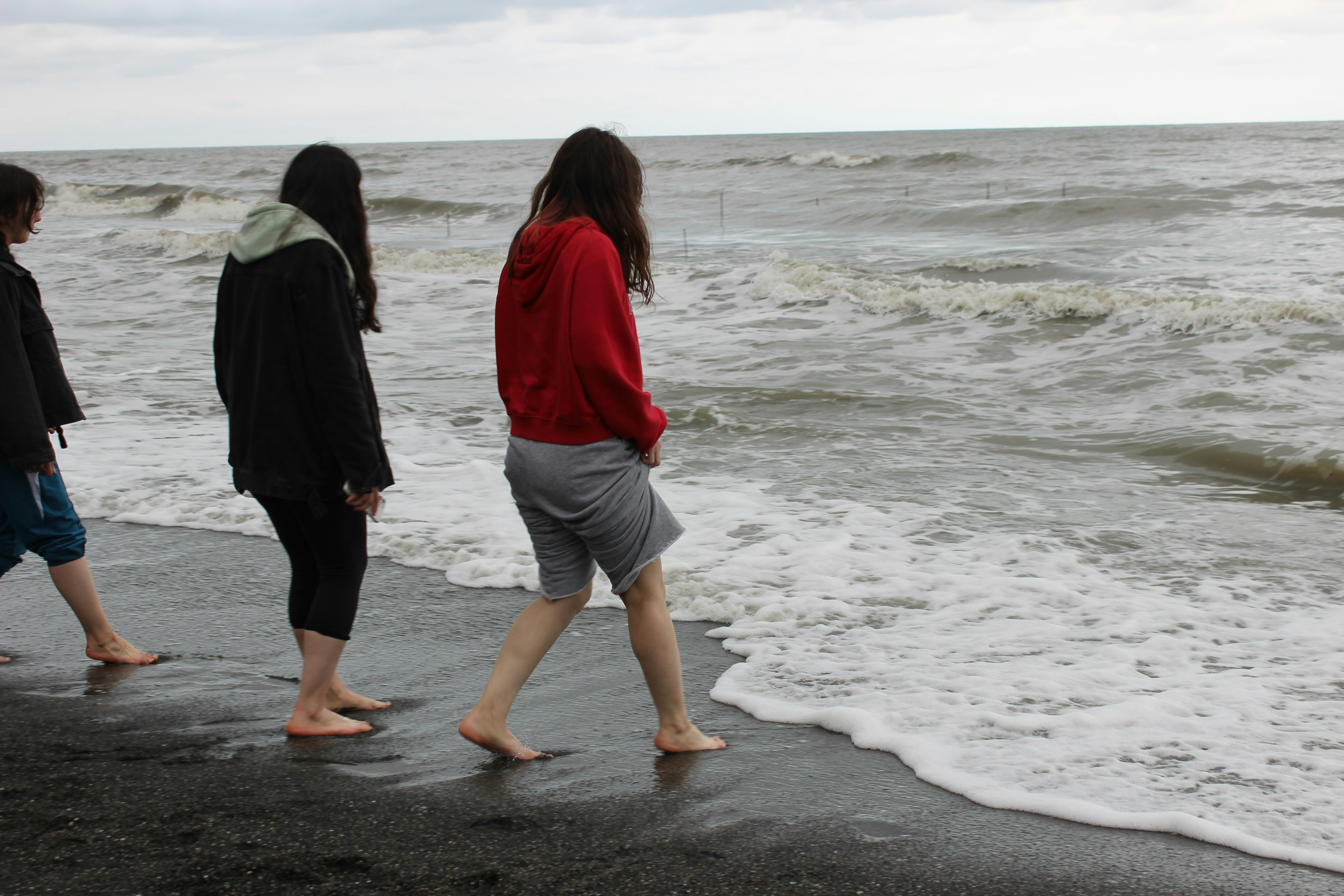 Three people walking on a dark sandy beach.