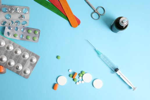 Medical supplies including pills, syringe, and scissors on blue.