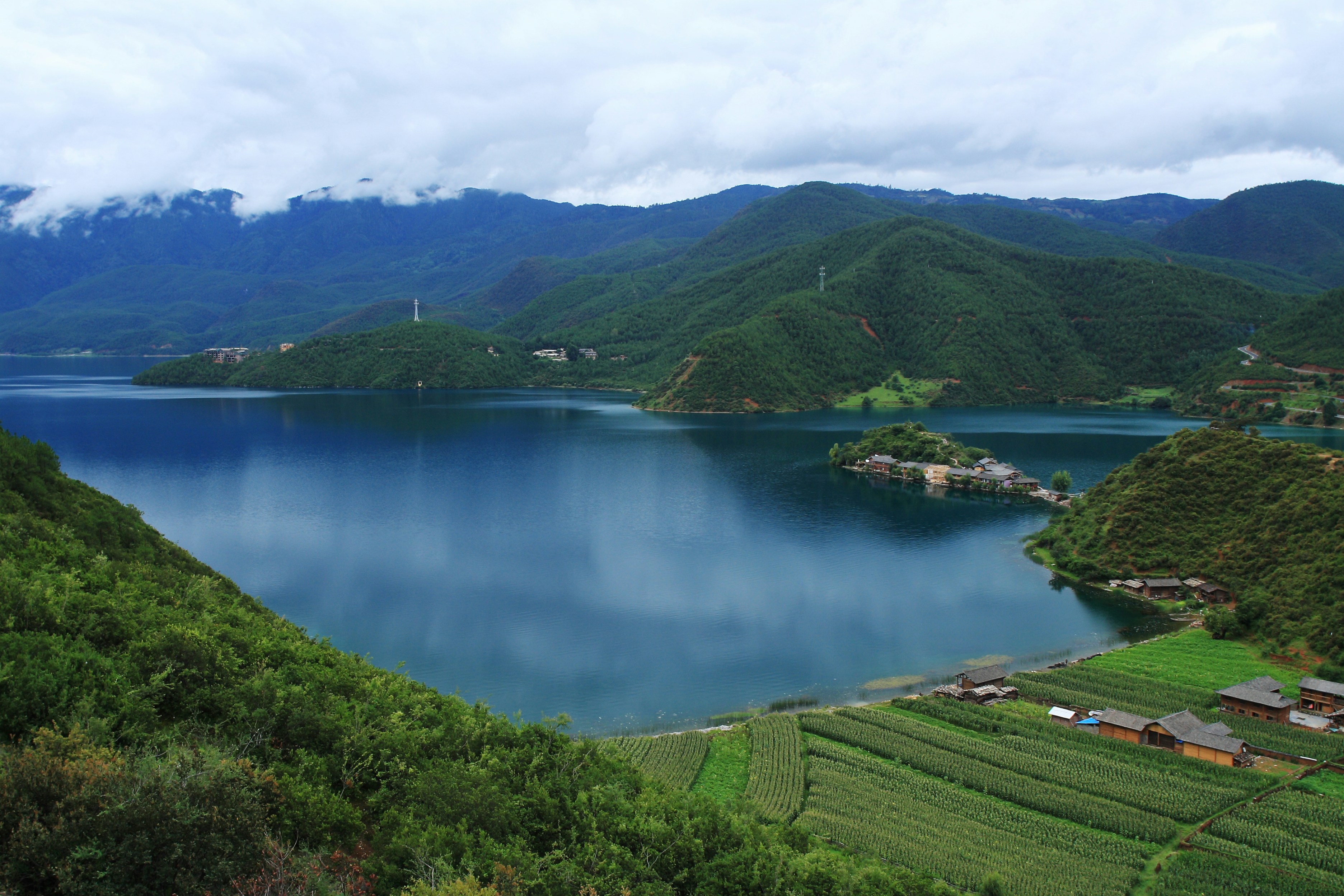Vast blue lake surrounded by green mountains and fields.