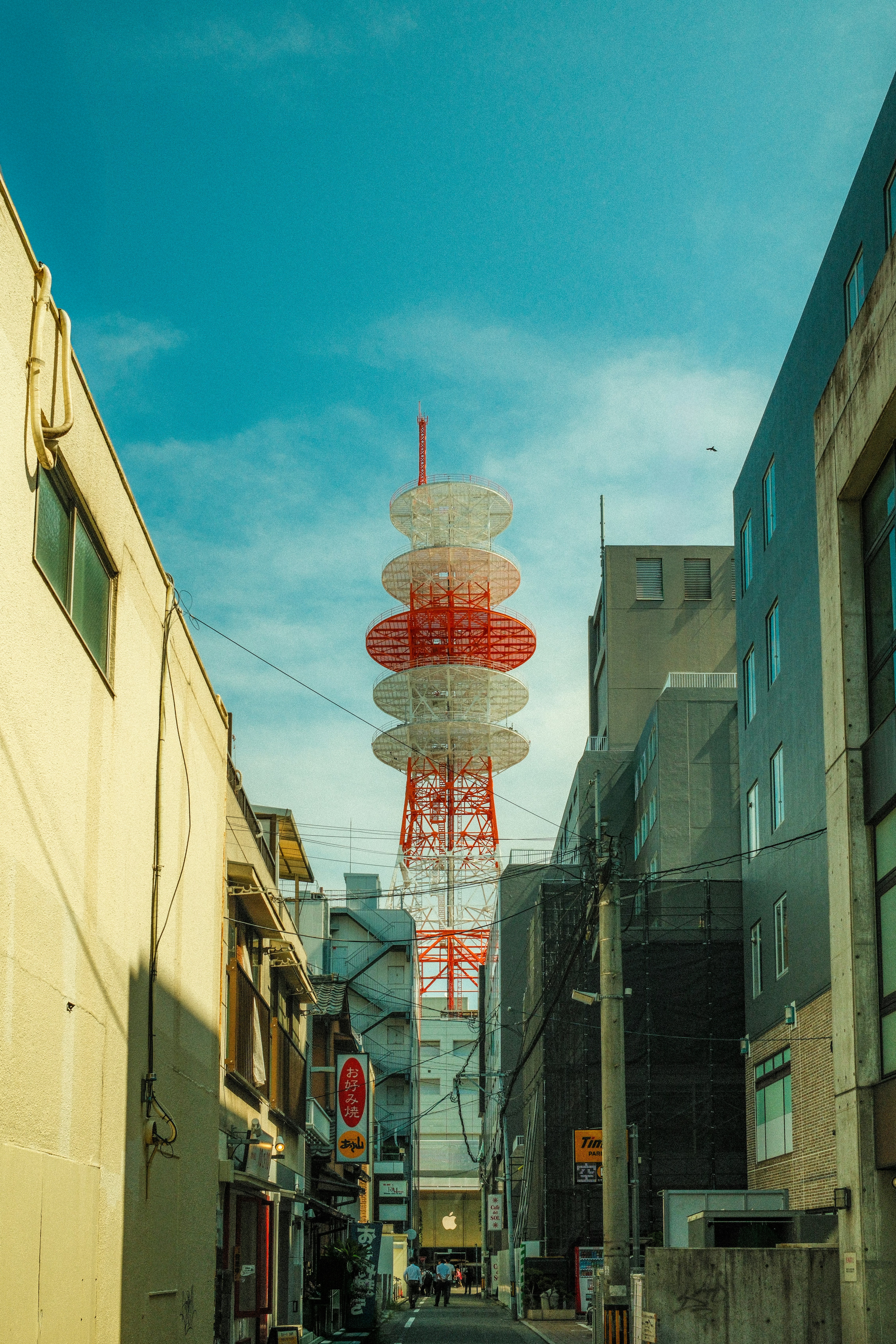 Tall red and white tower between buildings under blue sky