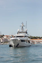 A large white yacht sails on blue water near buildings.