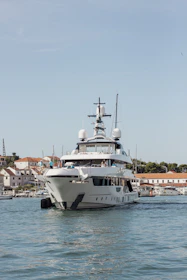 A large white yacht sails on blue water near buildings.