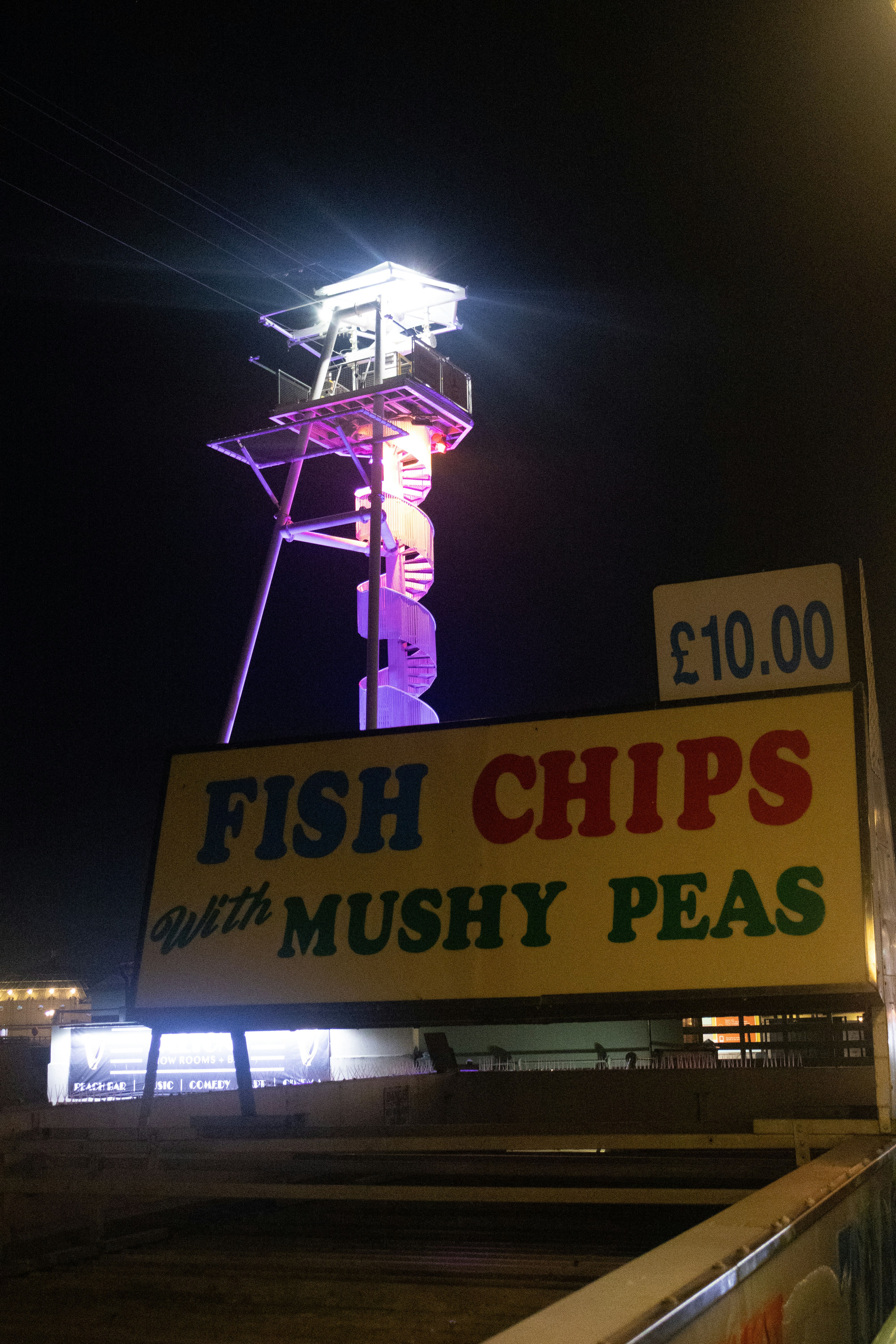 Fish and chips sign with tower at night.