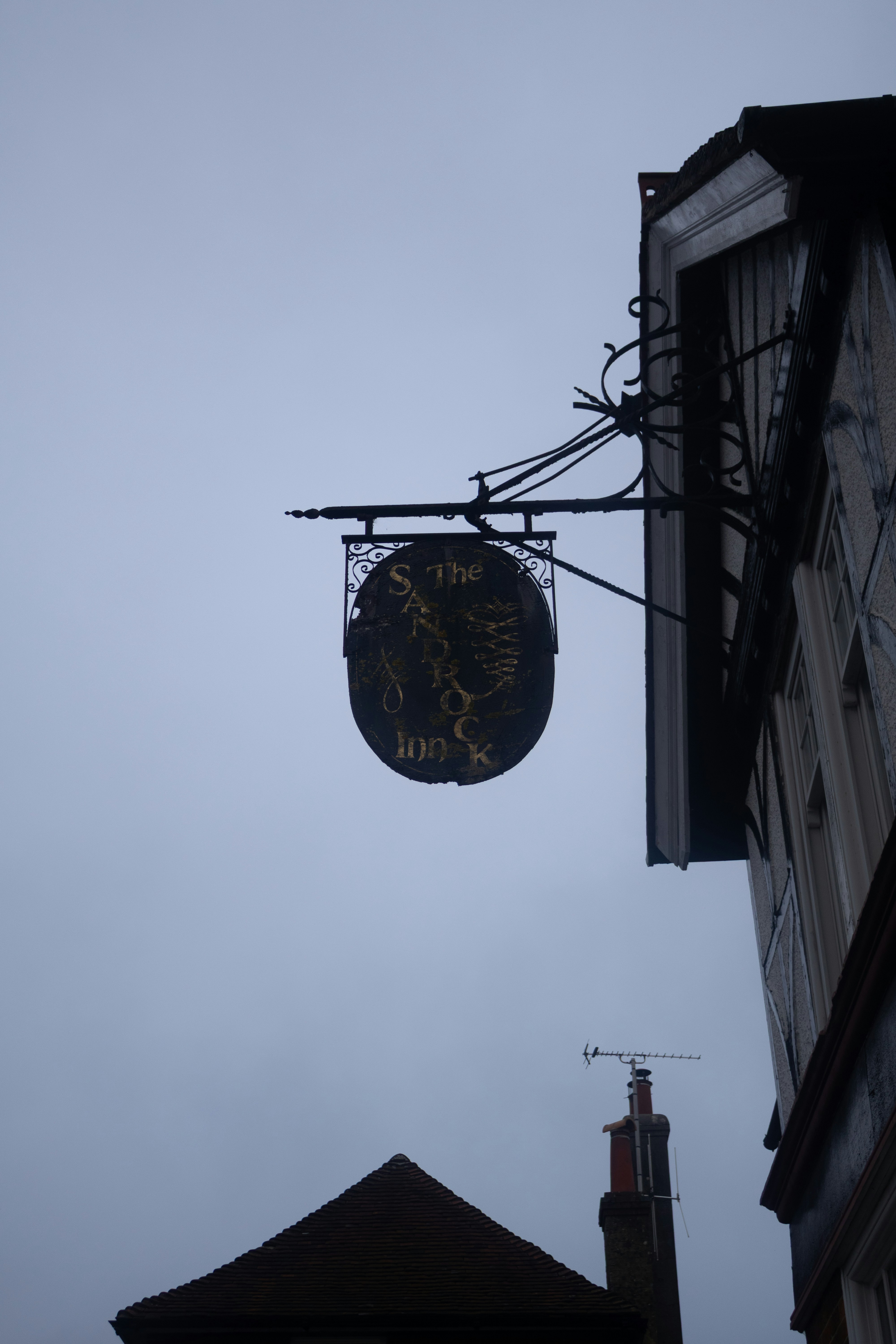 Ein altes Gasthausschild hängt an einem bewölkten Himmel.
