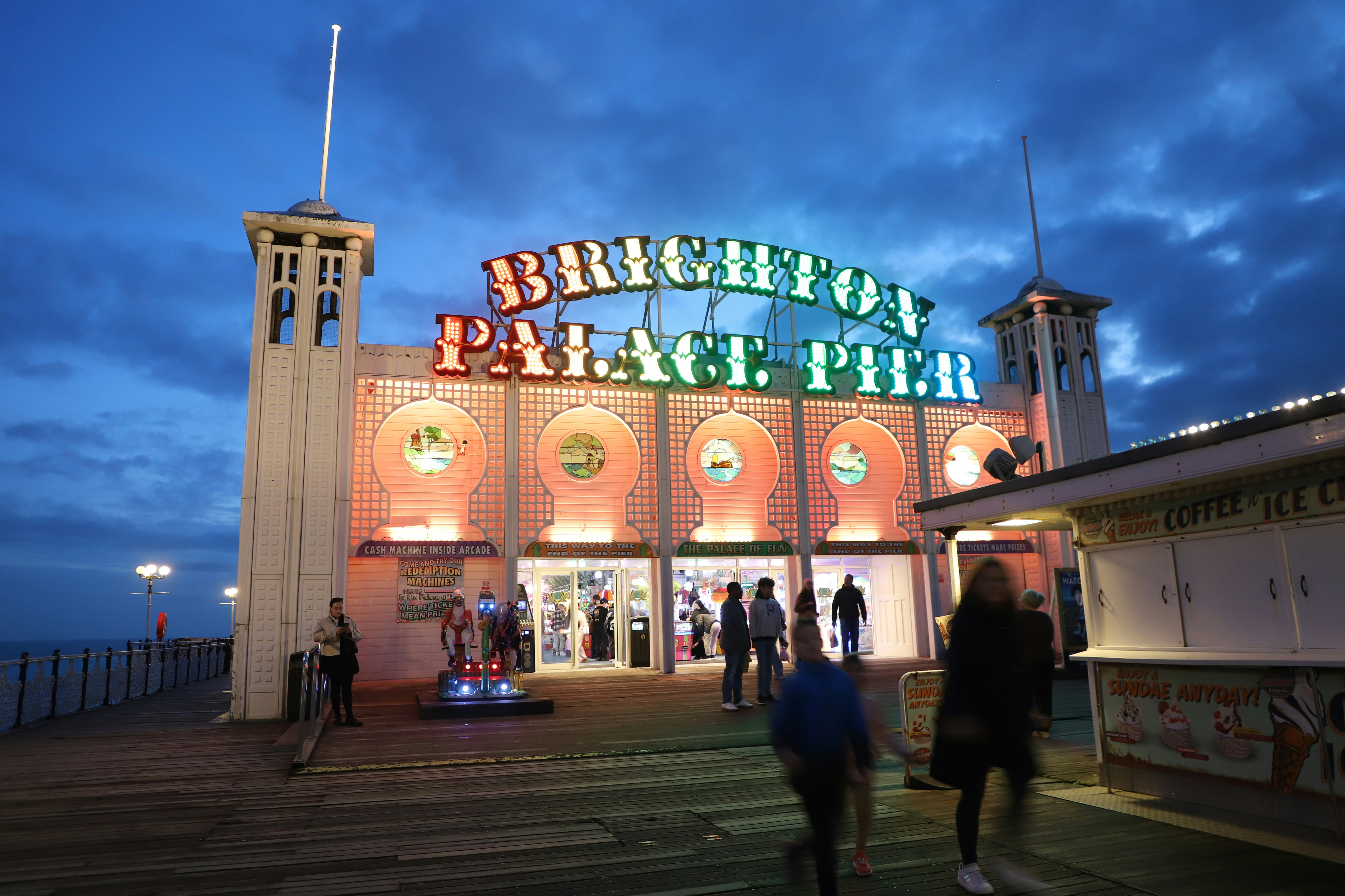 Brighton palace pier illuminated at dusk with people walking