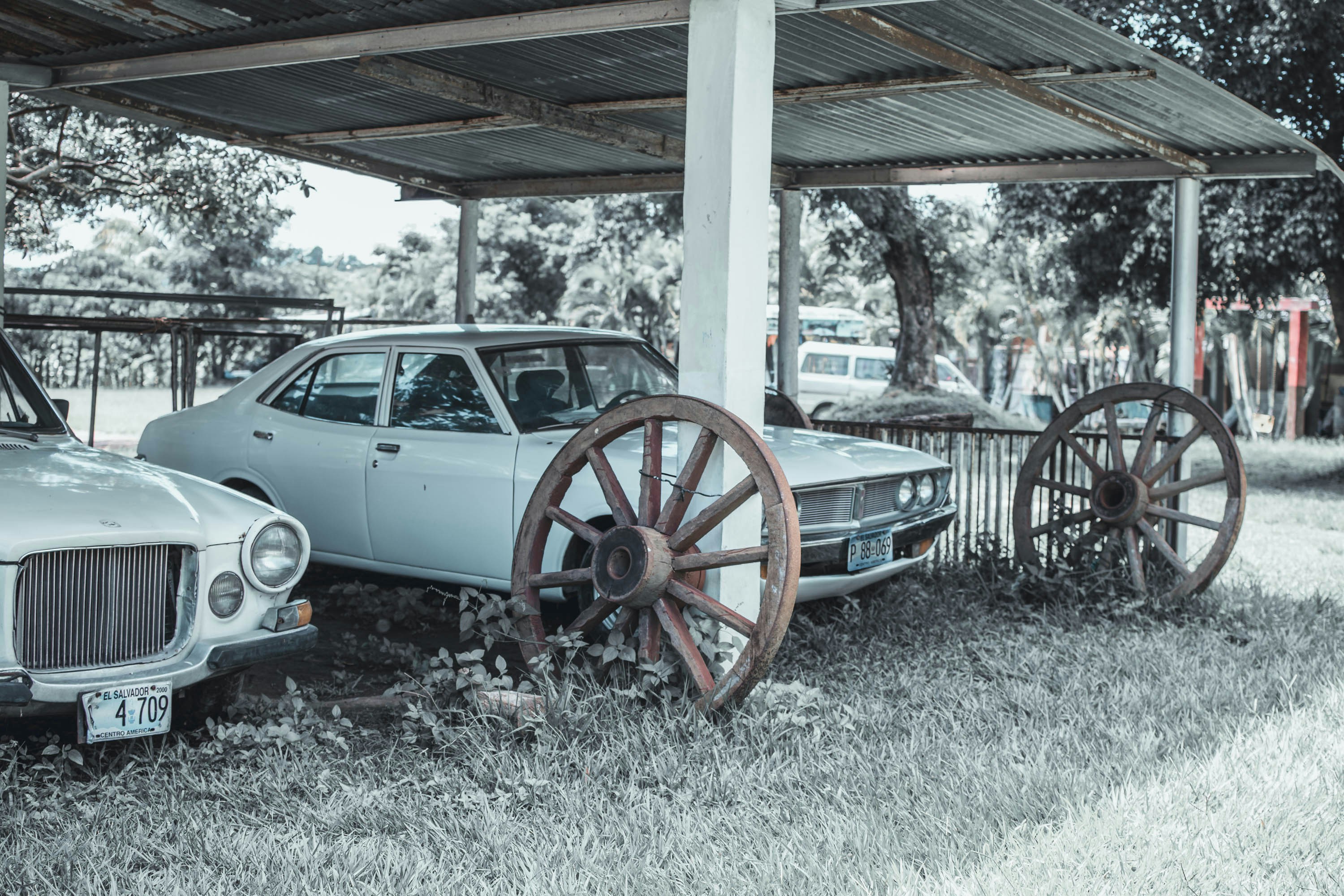 Two old cars and wagon wheels under shelter