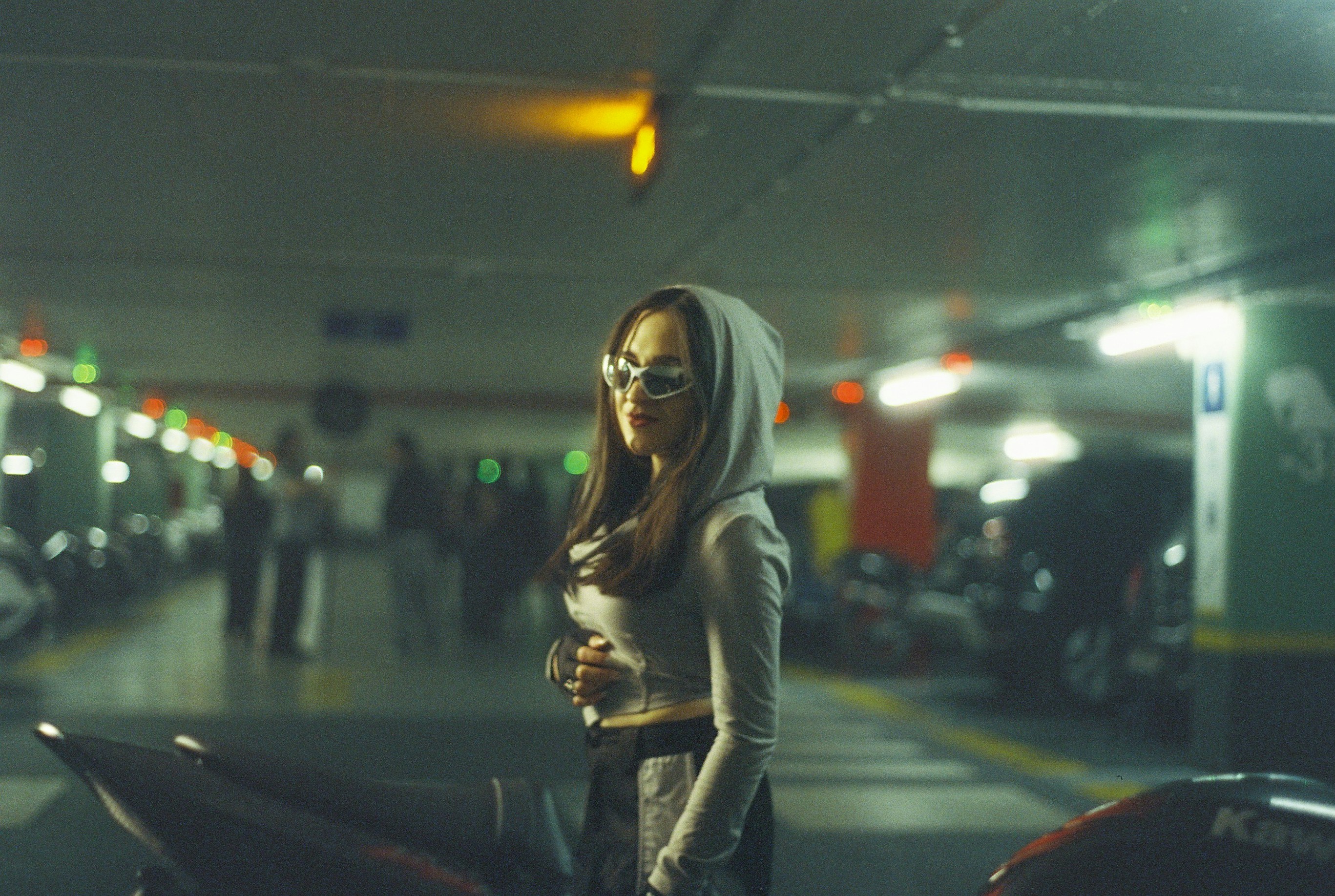 Woman in hoodie and sunglasses in parking garage.