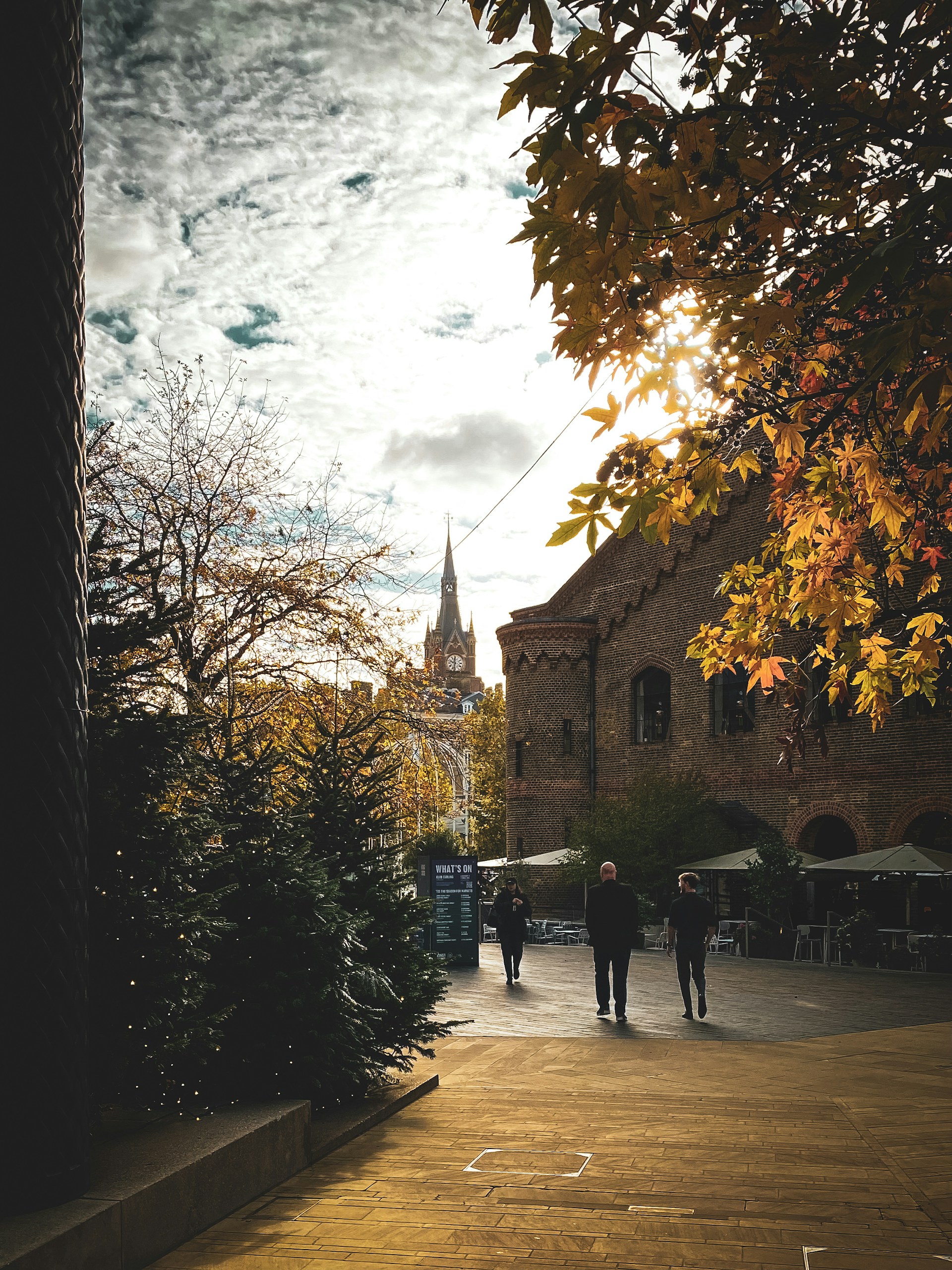 People walking past trees towards a church tower.