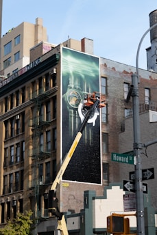 Workers install a large mural on a building facade.