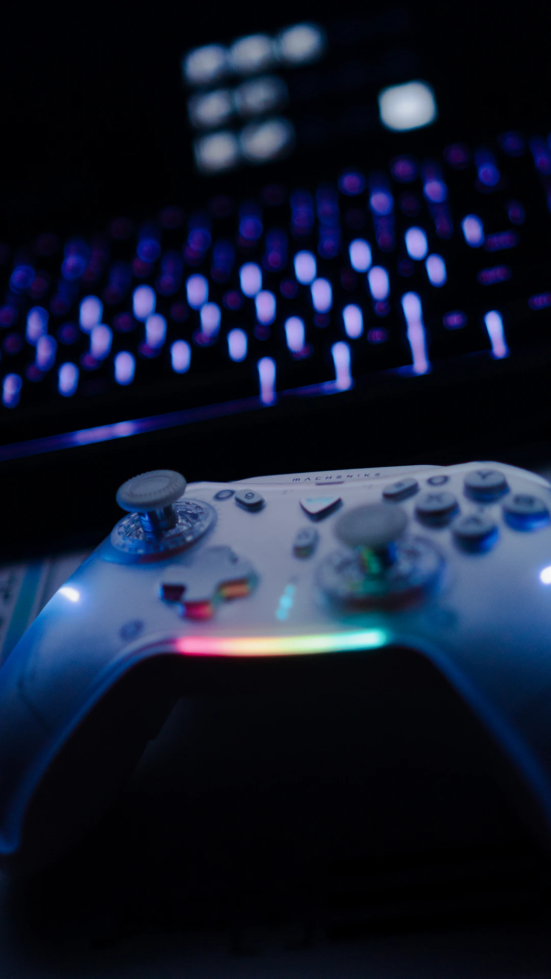A gaming controller beside an illuminated keyboard in a dark room