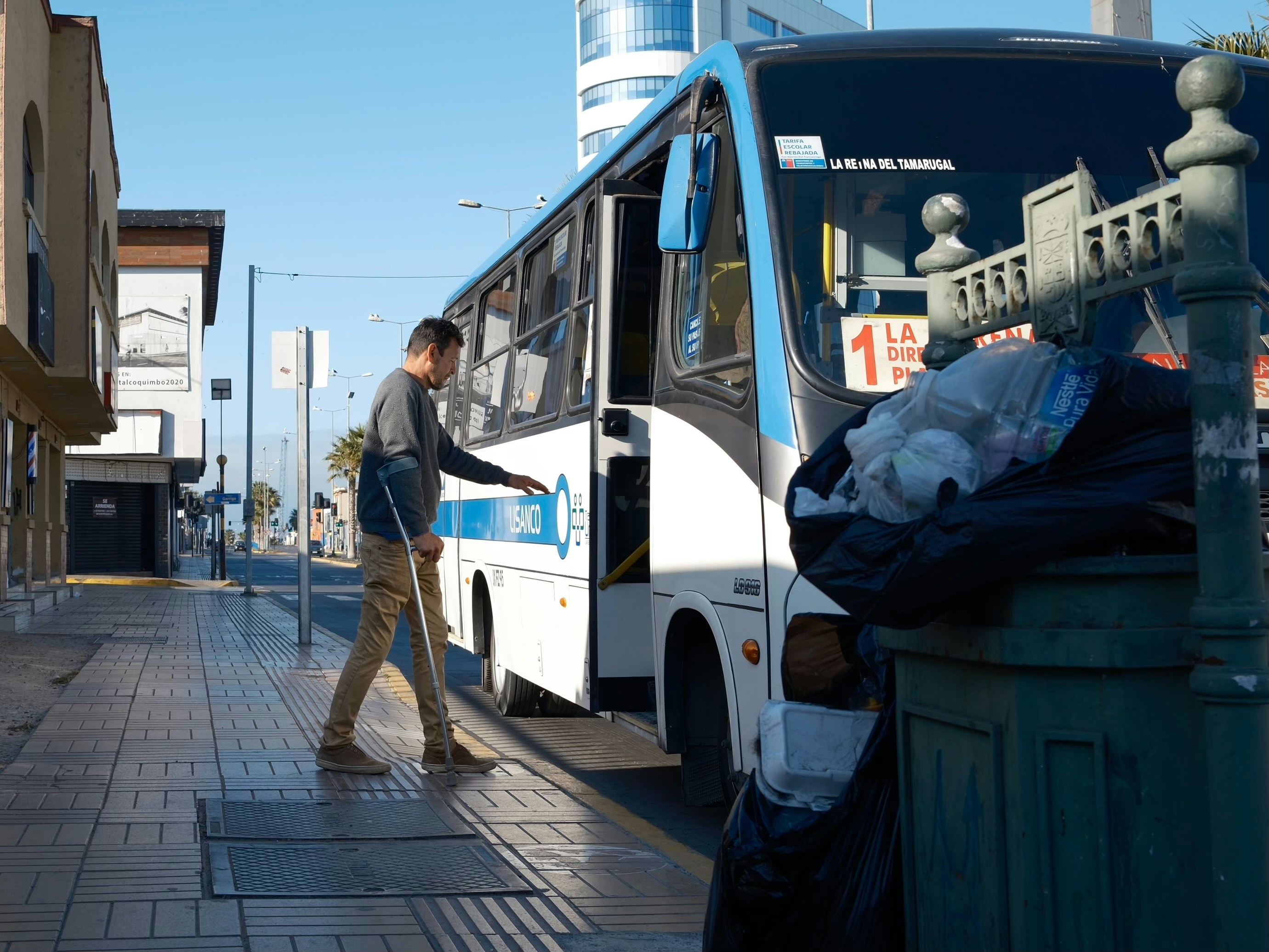 Man with cane boarding a bus on a sunny day