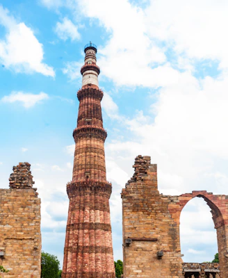 Historic qutub minar tower against a cloudy blue sky.