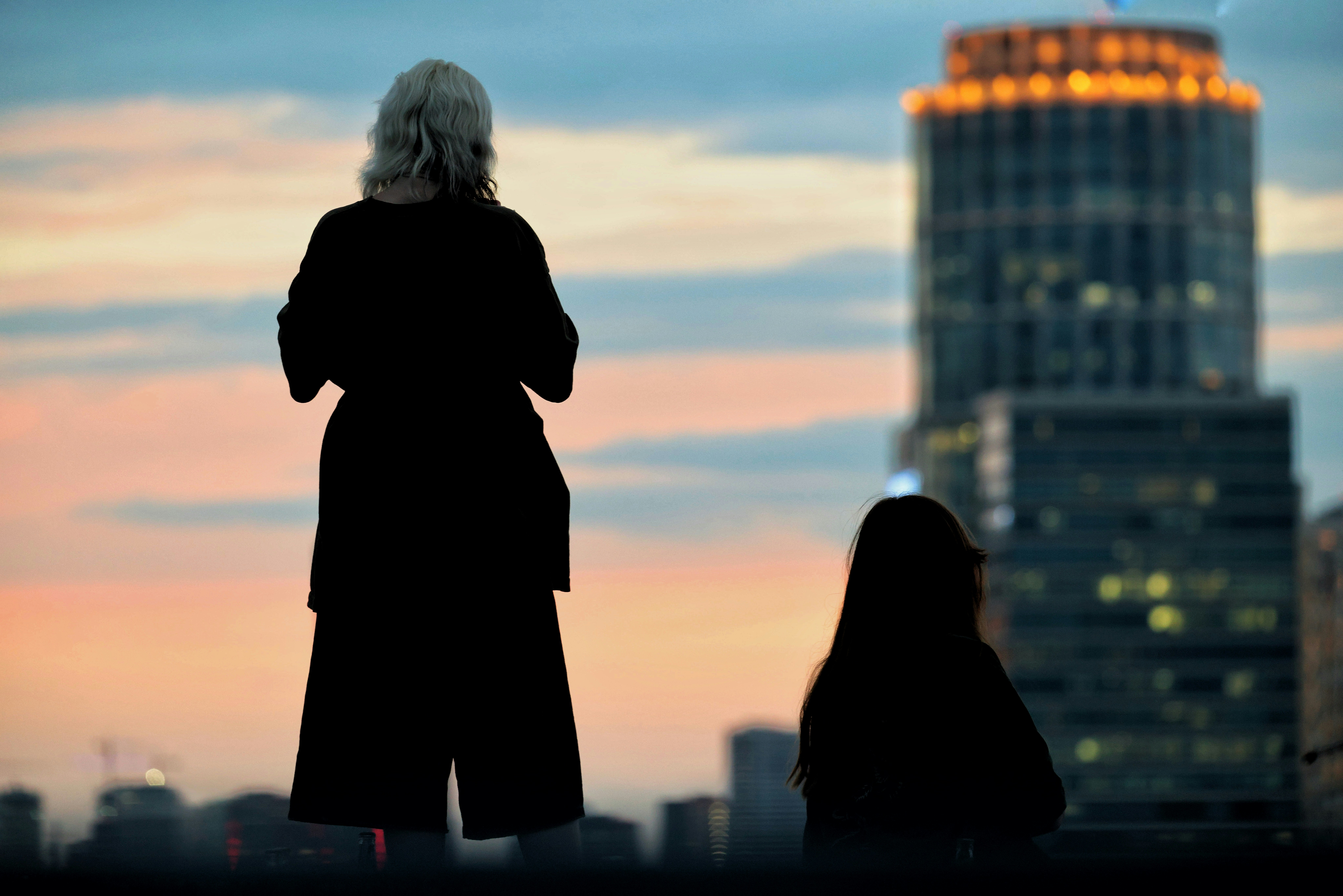Two people silhouetted against city skyline at dusk