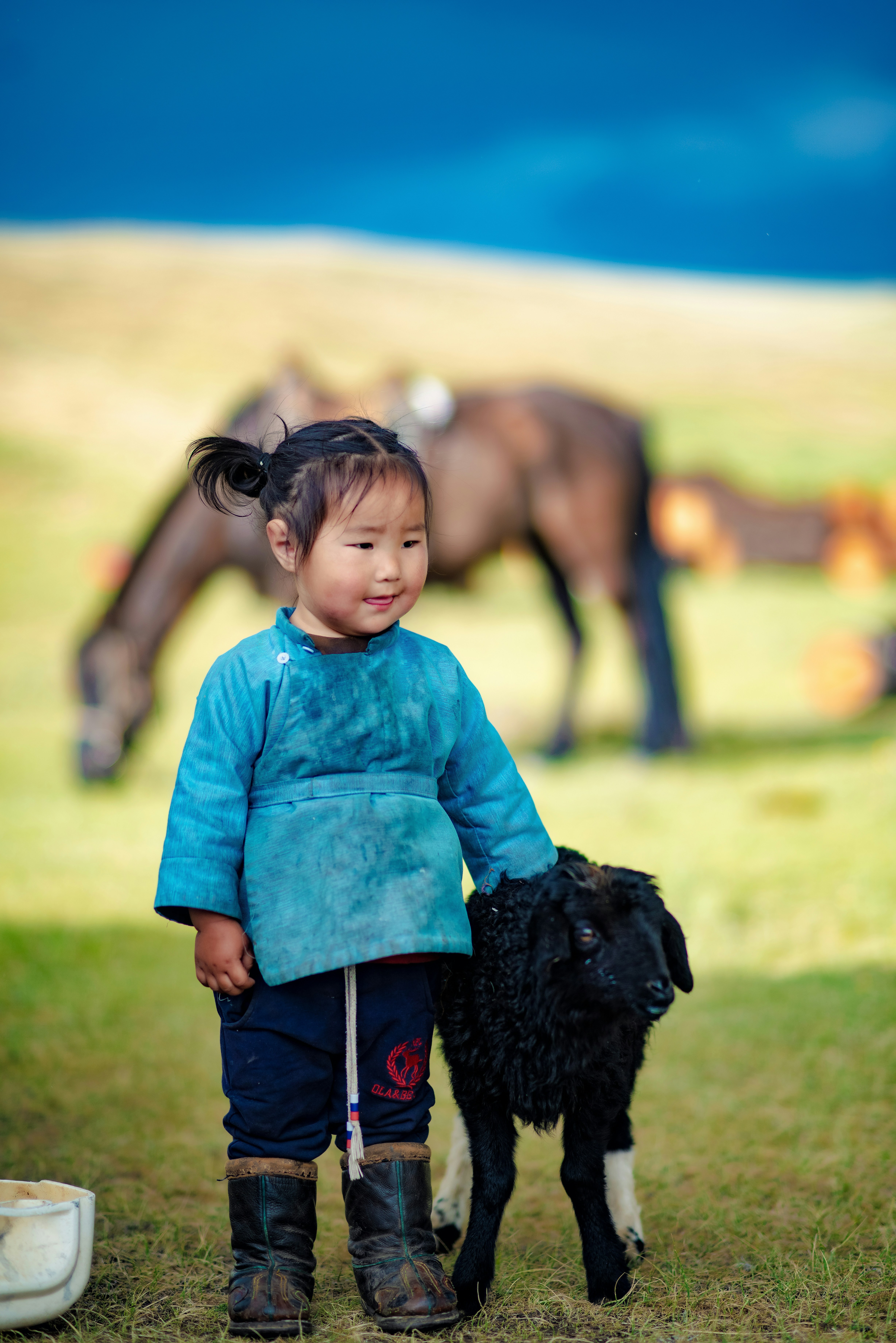 A young child stands with a black lamb.