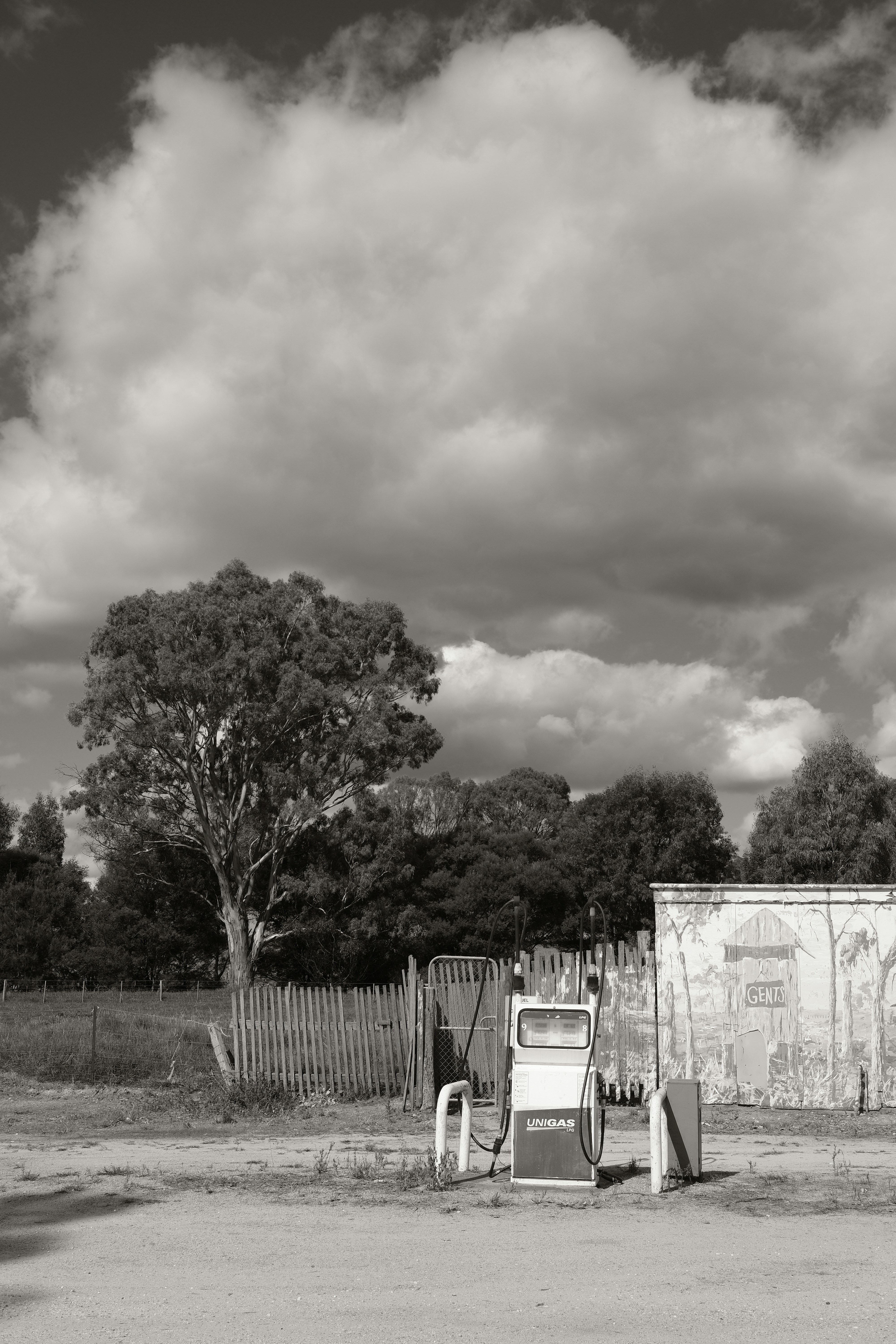 雲の下、風化した建物の近くに建つヴィンテージのガソリンポンプ